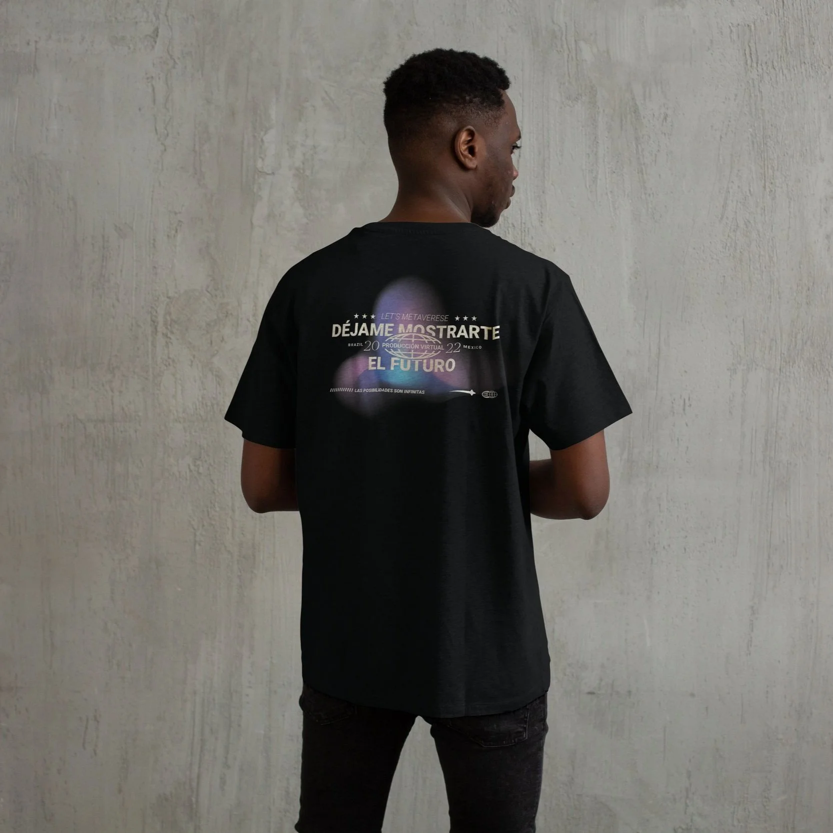 A person viewed from behind wearing a black T-shirt with colorful text and graphics, standing in front of a plain, textured wall.