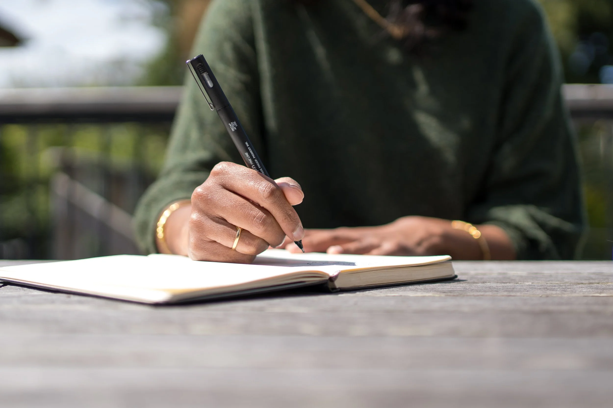 Person writing in notebook outdoors on wooden table