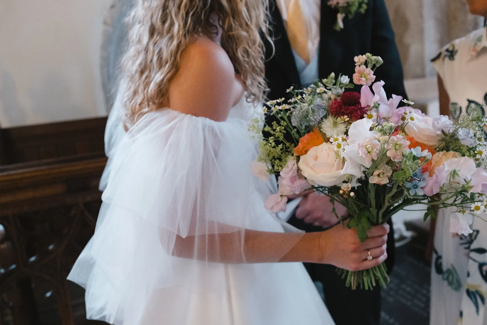 A woman in a white dress holding a large bouquet of flowers during a wedding ceremony.