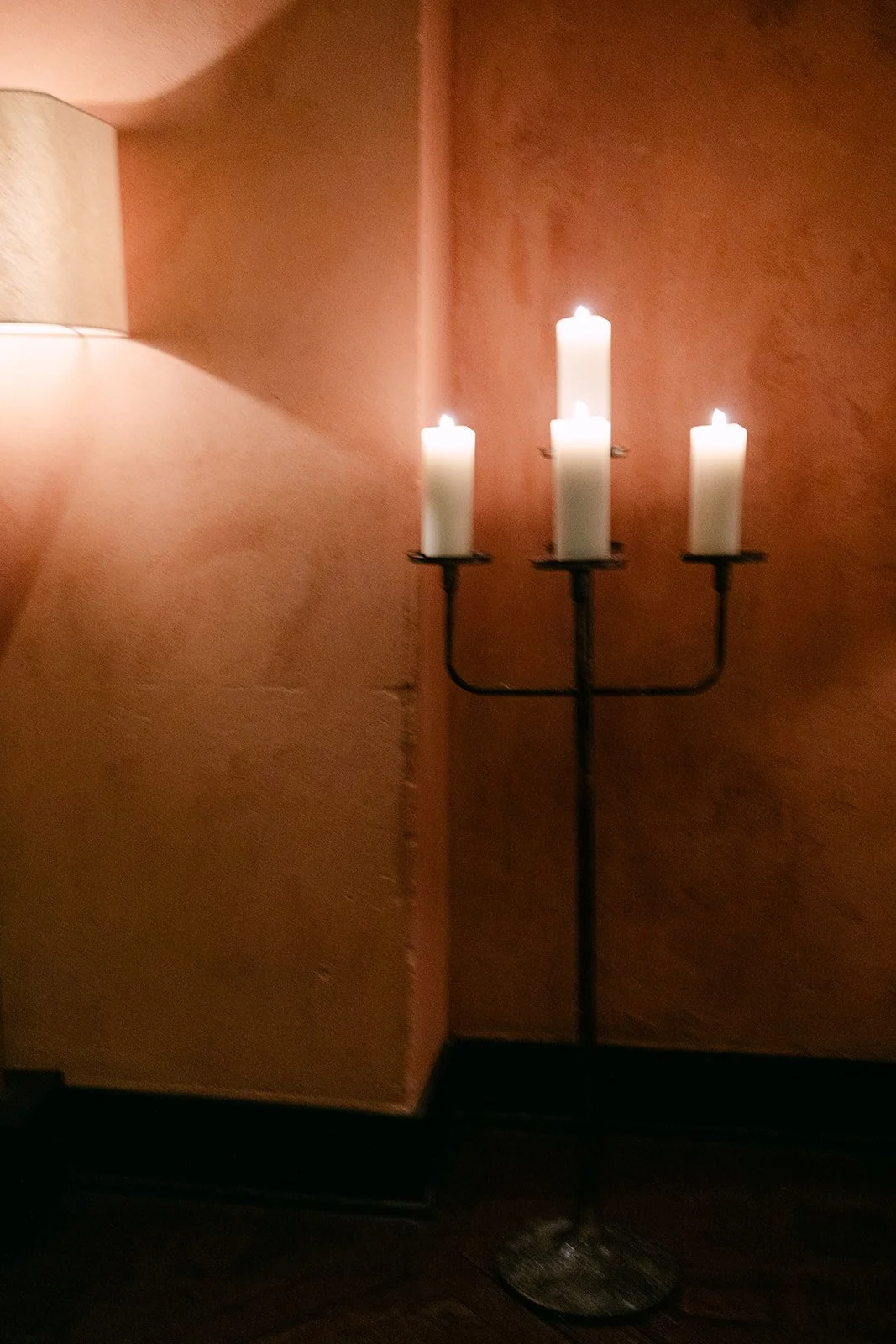 Candle stand with four white lit candles against a textured warm-colored wall.