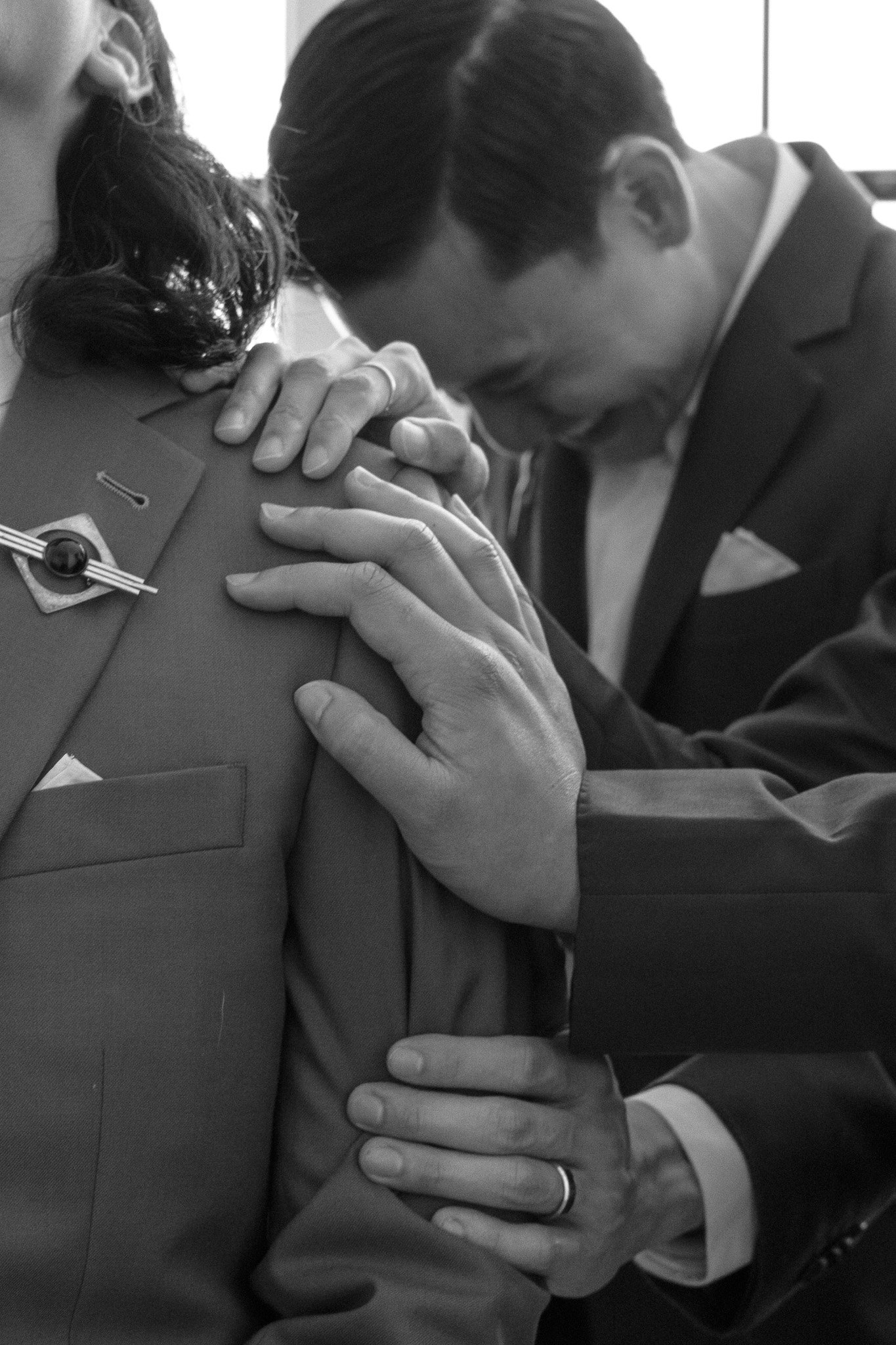 Black and white photo of people in suits, some with hands on another's shoulder, conveying a supportive gesture.