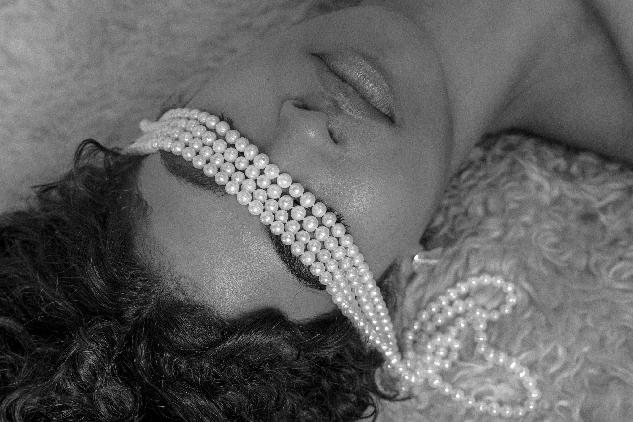 Person lying down with pearl strands over their eyes in black and white.