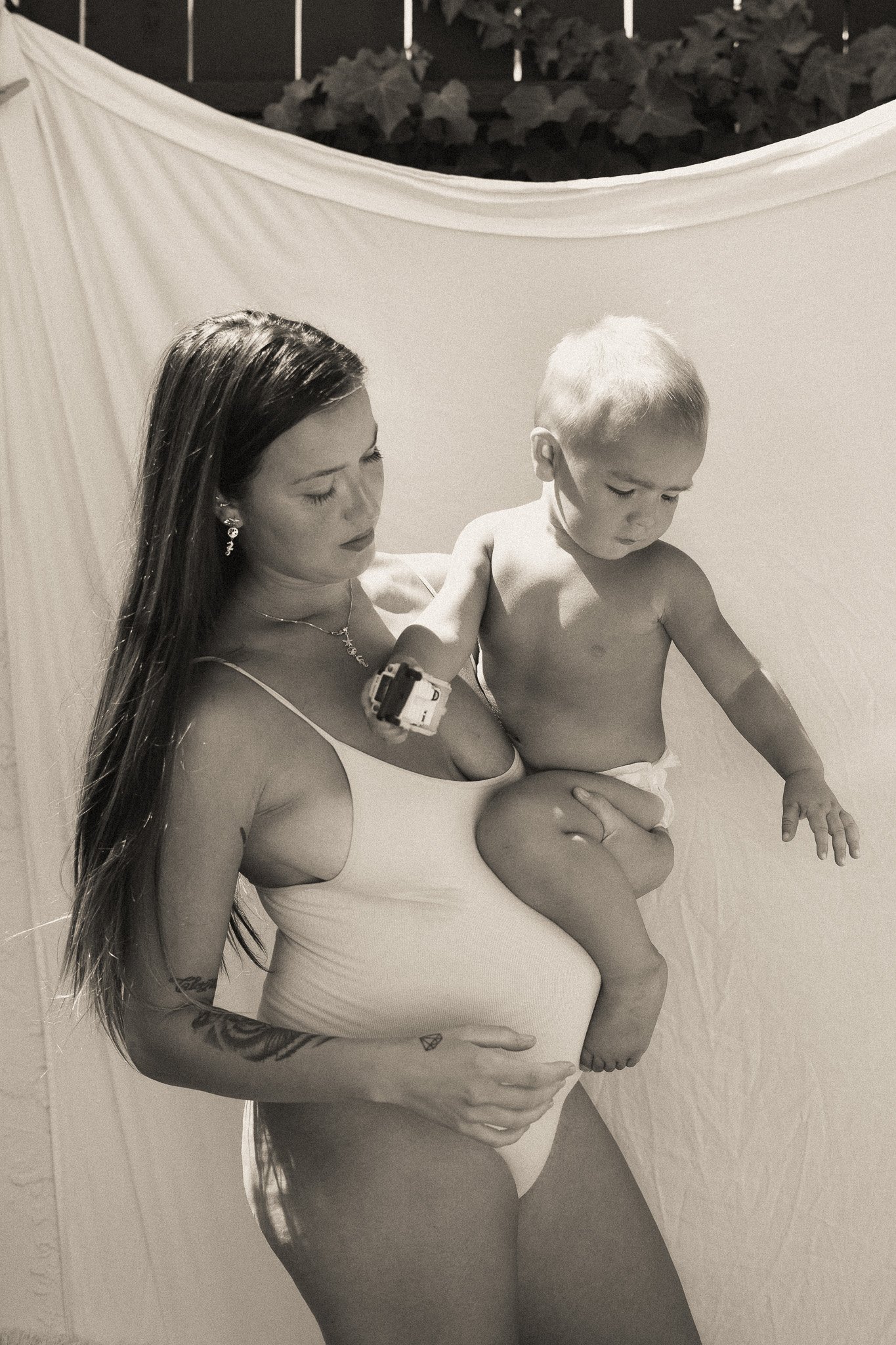 A black and white photo of a woman in a swimsuit holding a baby wearing a diaper.