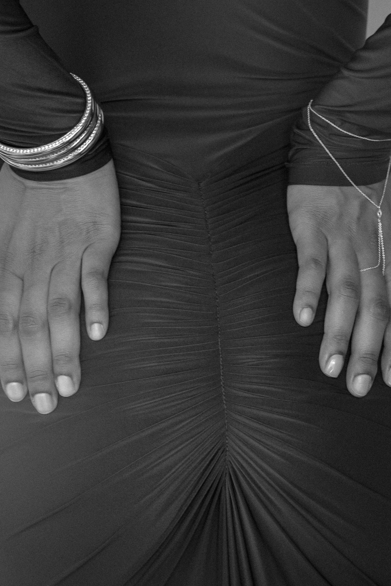Close-up of hands on black ruched fabric with silver bracelets and chain jewelry.