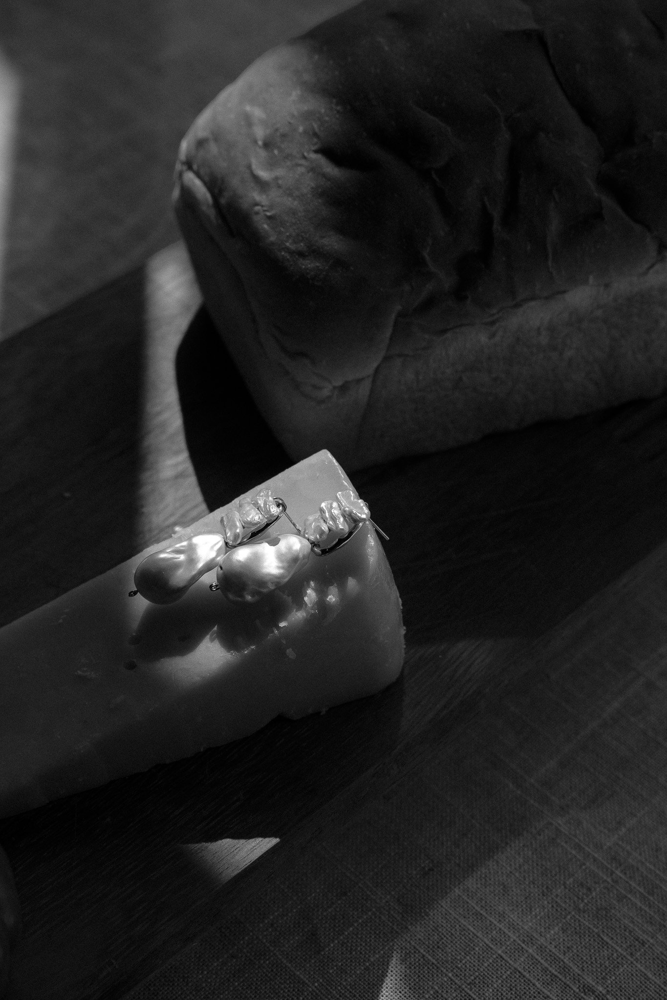 Black and white photo of a loaf of bread and a wedge of cheese with decorative elements placed on it, on a wooden surface.