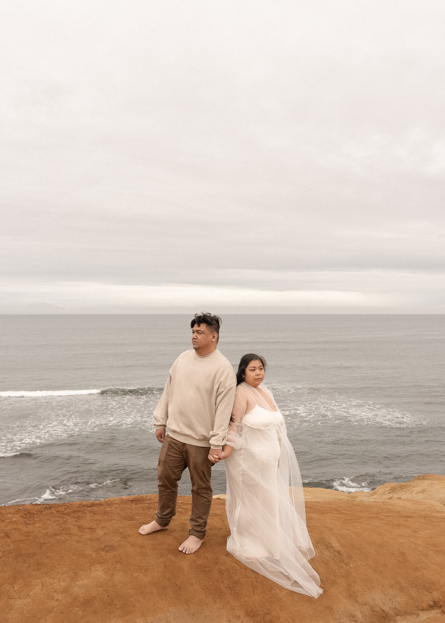 Couple holding hands on a rocky coastline with ocean in background.