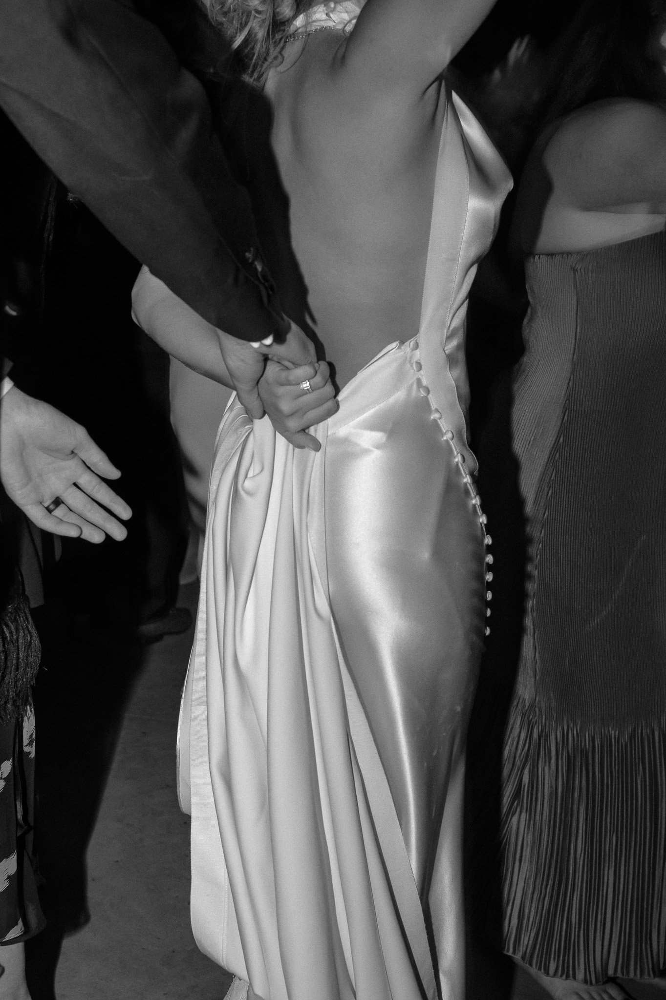 Close-up of a person in a backless dress holding hands, with a satin texture and button detailing on the side.