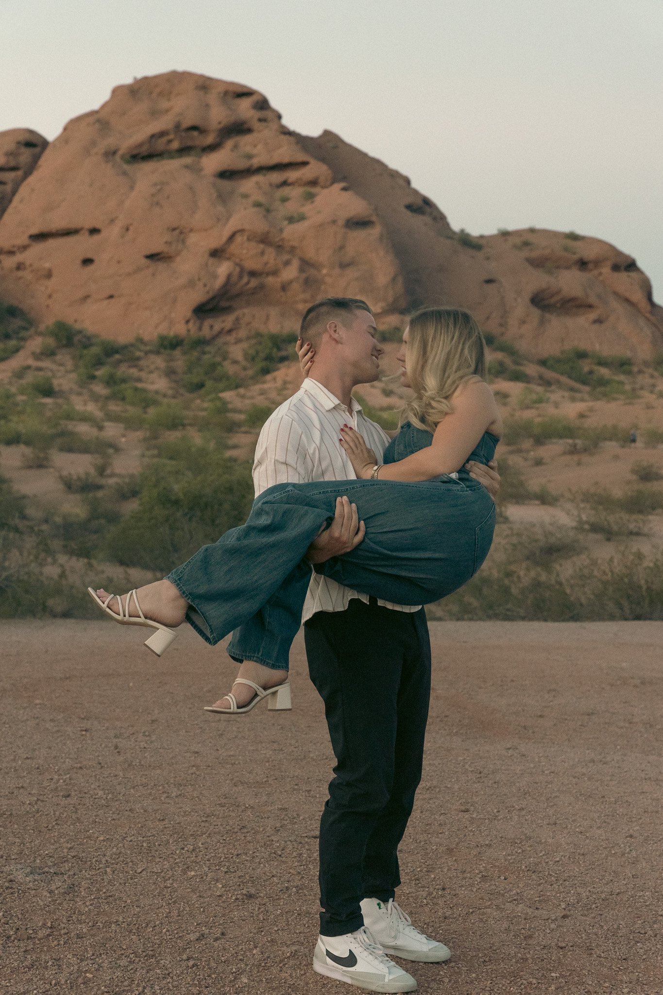 Man holding a woman in a loving embrace with rocky desert landscape in the background.