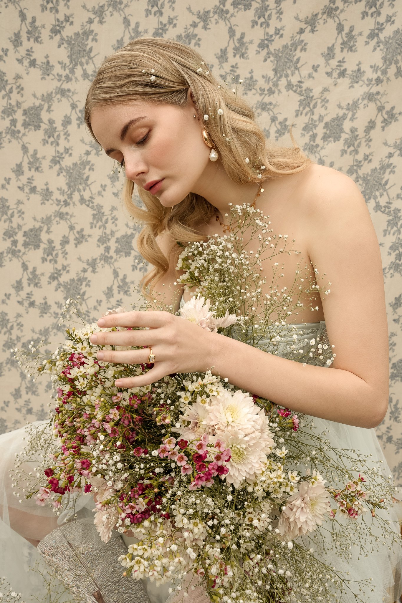 Woman holding a large bouquet of flowers with pastel and floral wallpaper background.