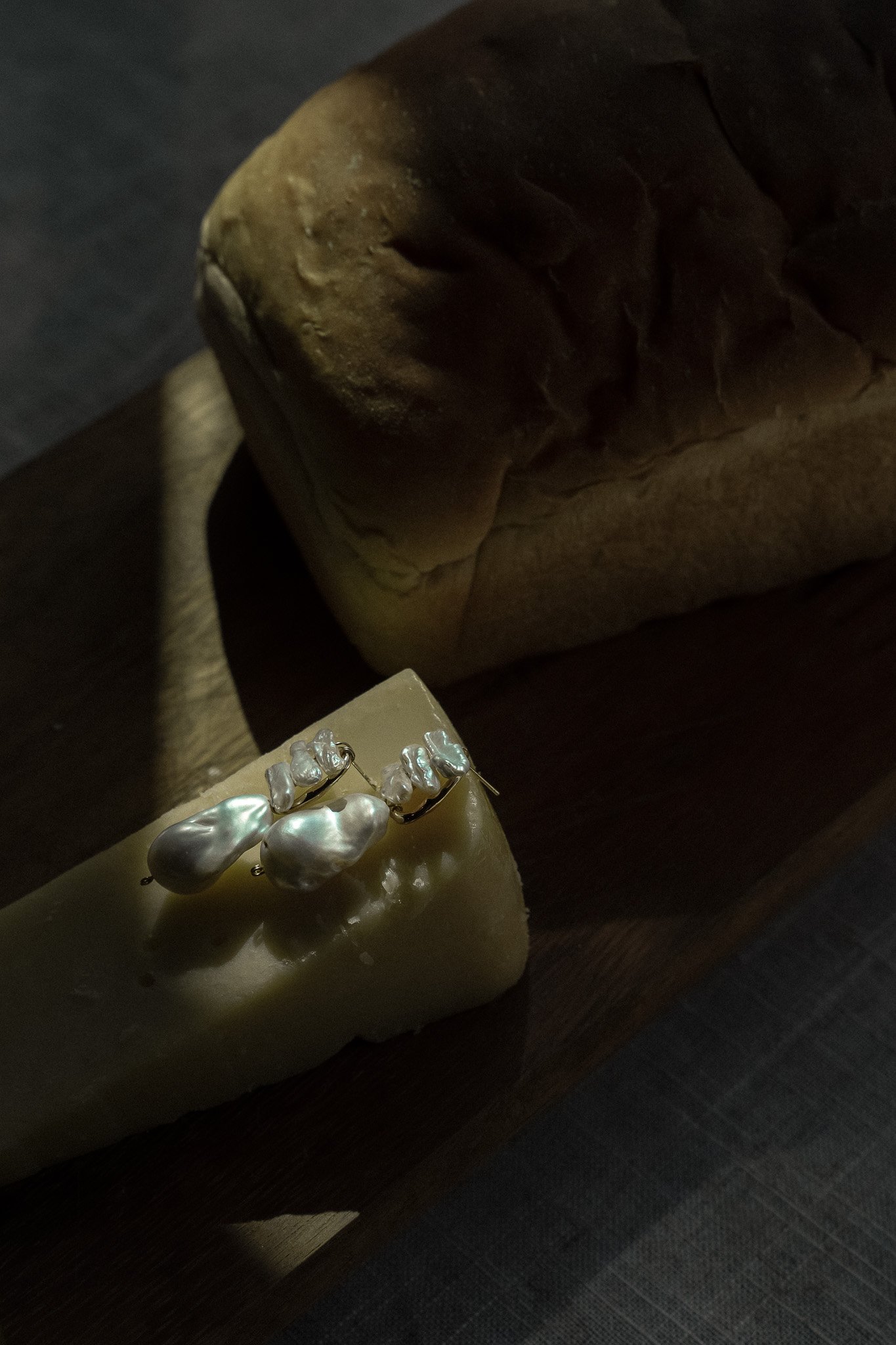 Bread loaf and cheese with pearl earrings on wooden board