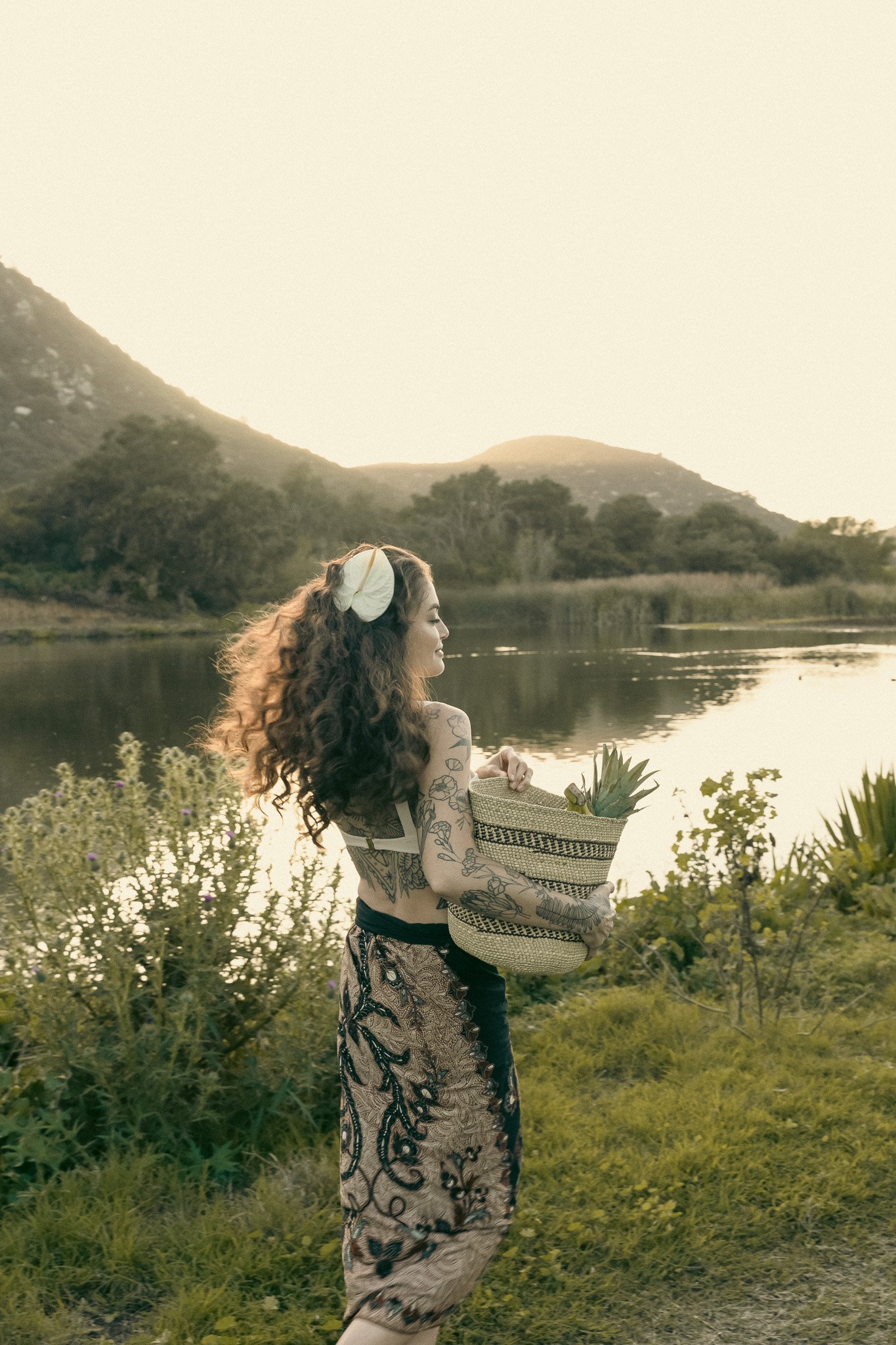 Woman with tattoos holding a woven basket by a lake
