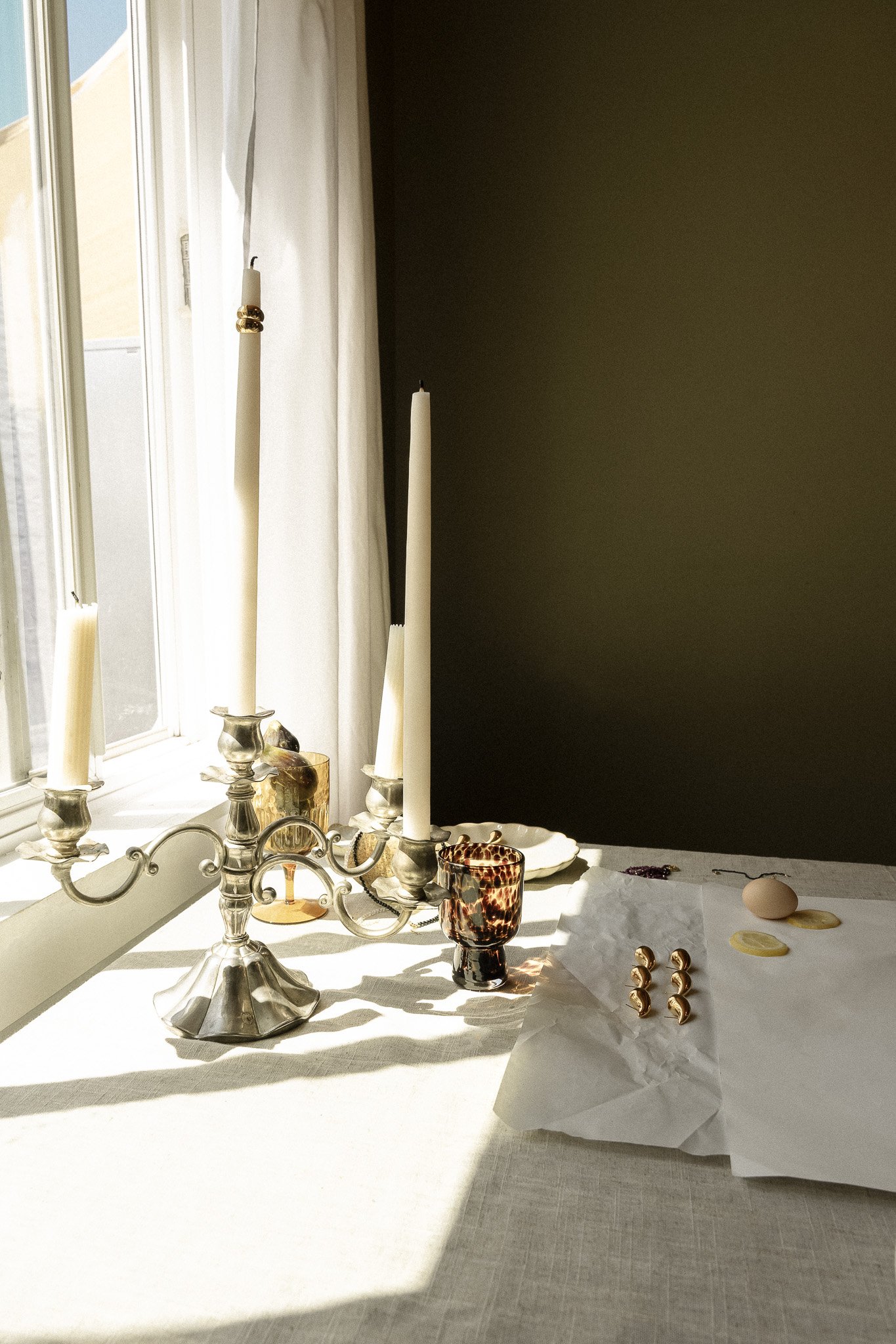 Table setting with white candles in a silver candelabra, amber glass, and lemons on a white tablecloth