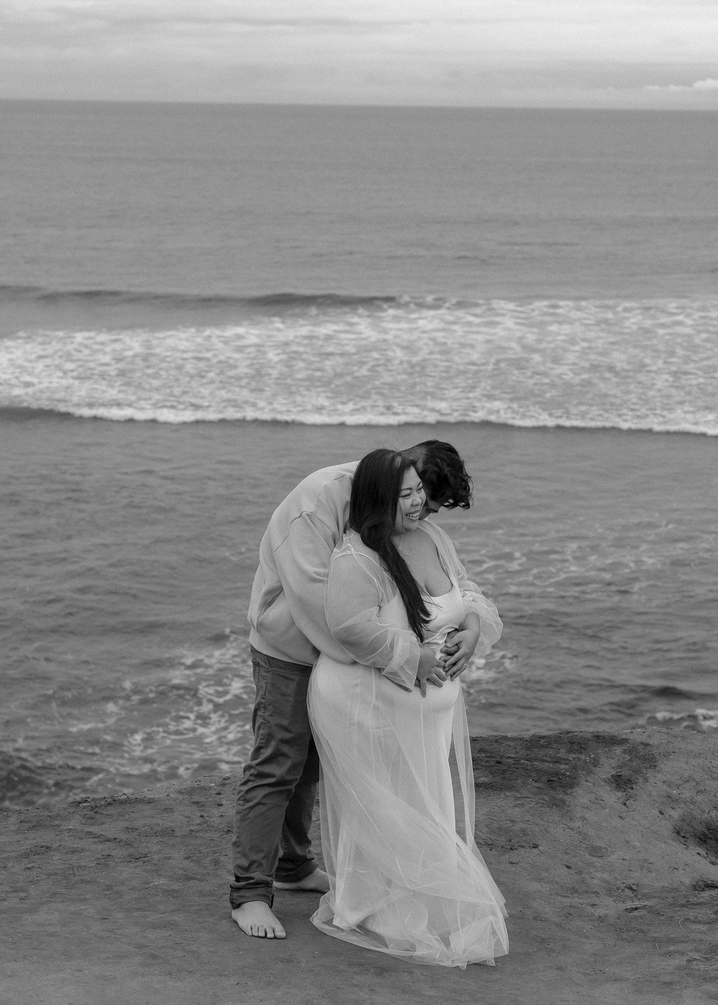 Couple embracing near ocean shore, black and white photo.
