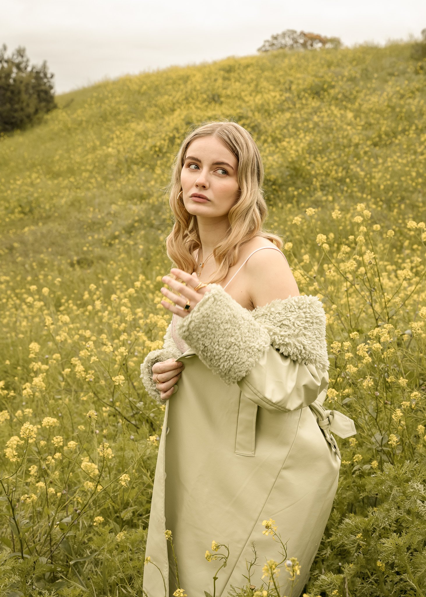 Woman in a field of yellow flowers wearing a green coat