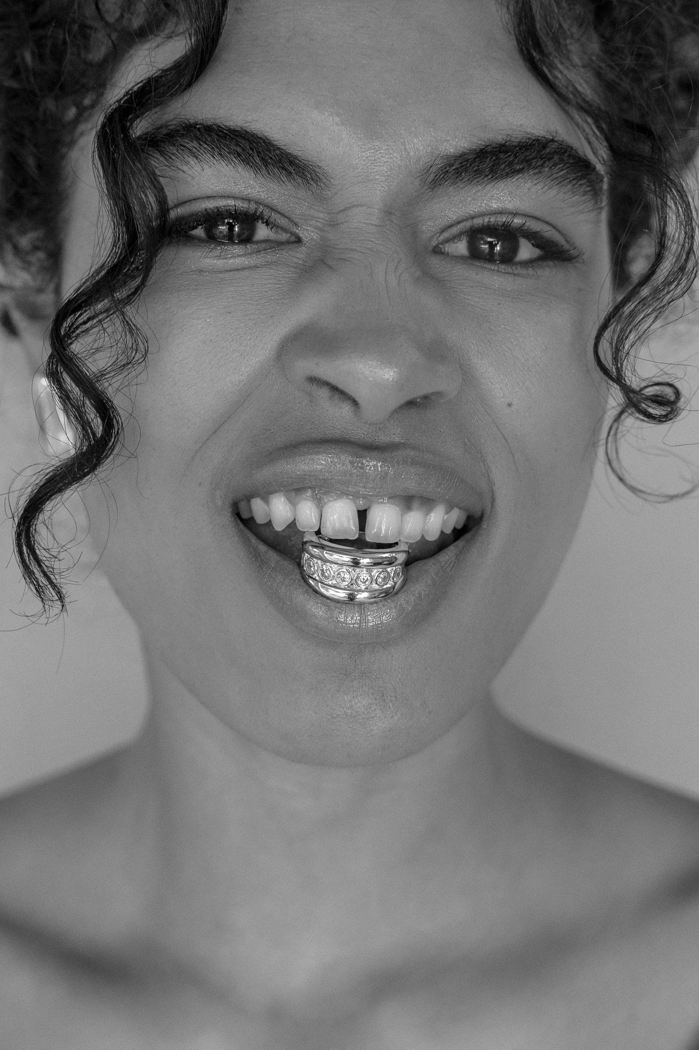 Close-up of a person with curly hair wearing a lip ring and showcasing a grill on their bottom teeth.
