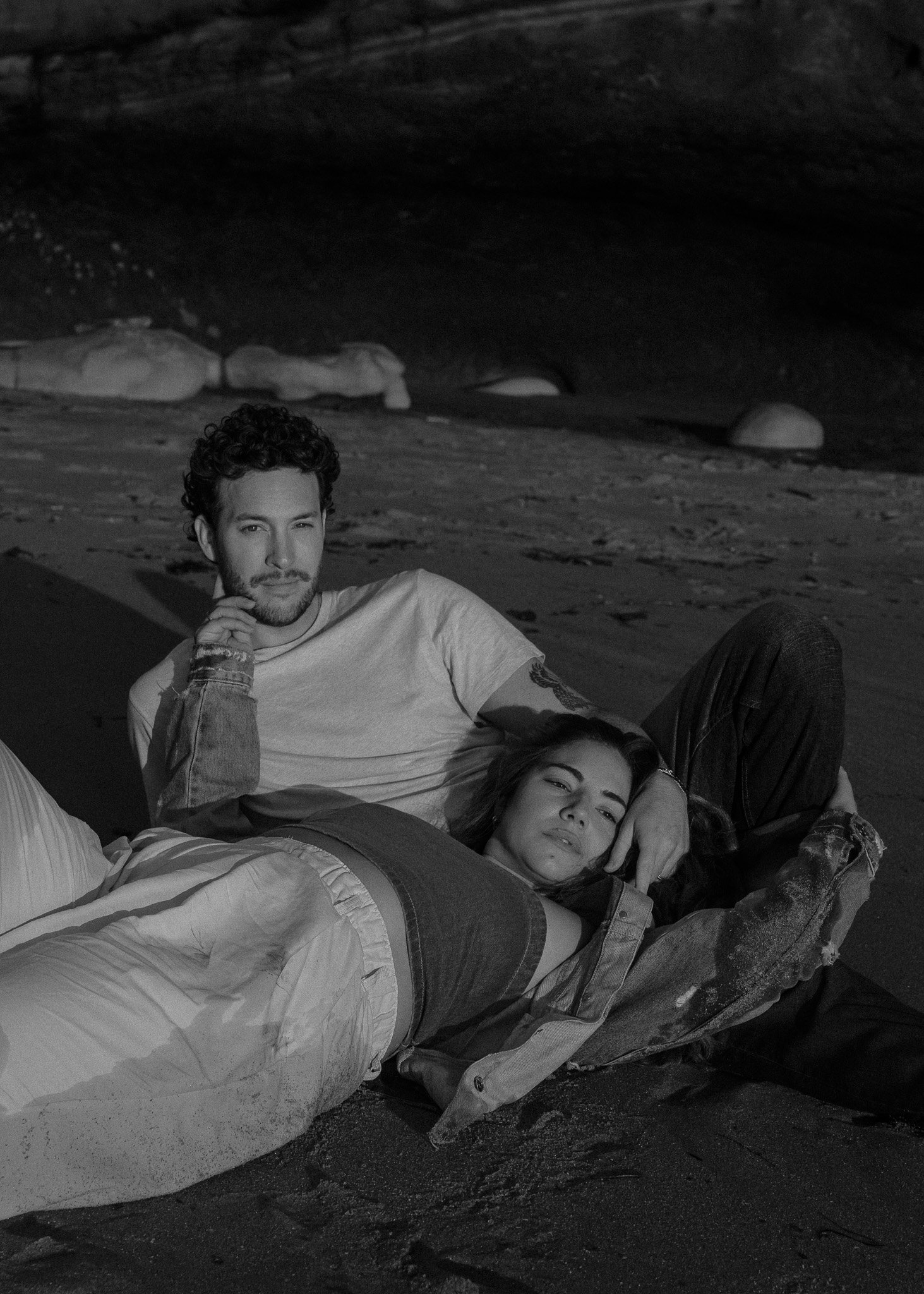 Black and white photo of a man and woman relaxing on a beach, with the woman lying on the man's lap.
