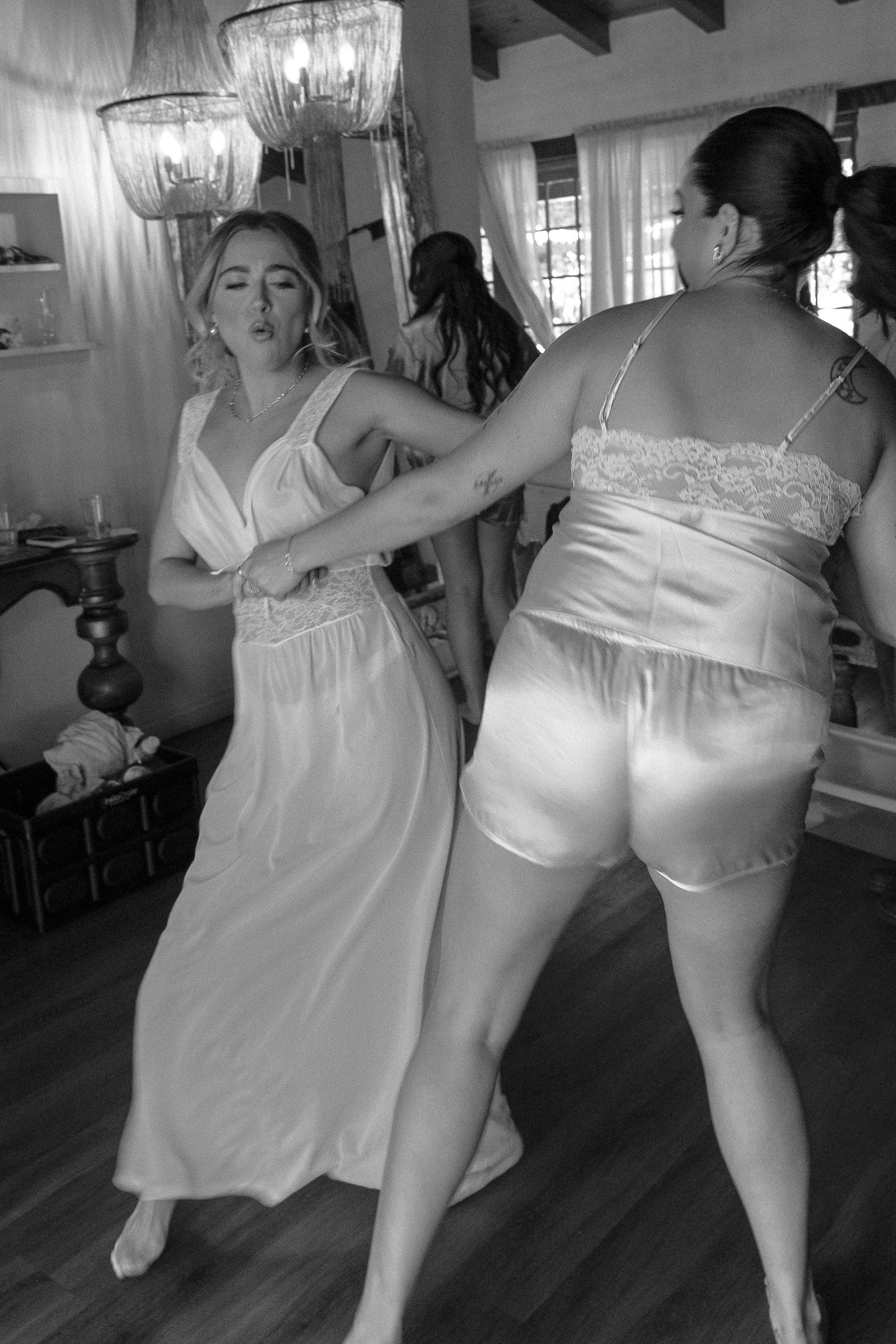 Women dancing indoors in dresses, black and white photo.