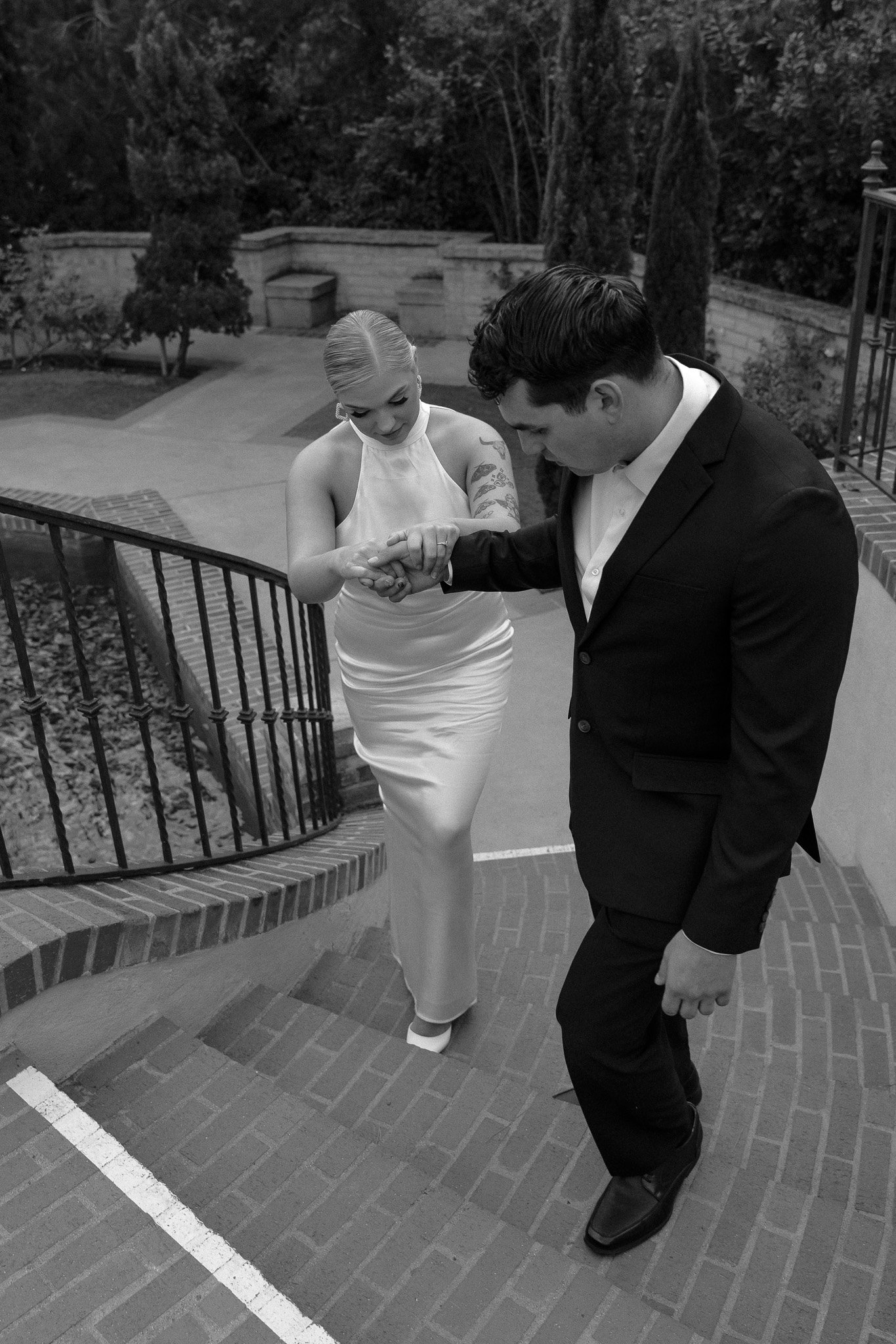 A man and woman in formal attire walking up brick stairs, with the man holding the woman's hand.
