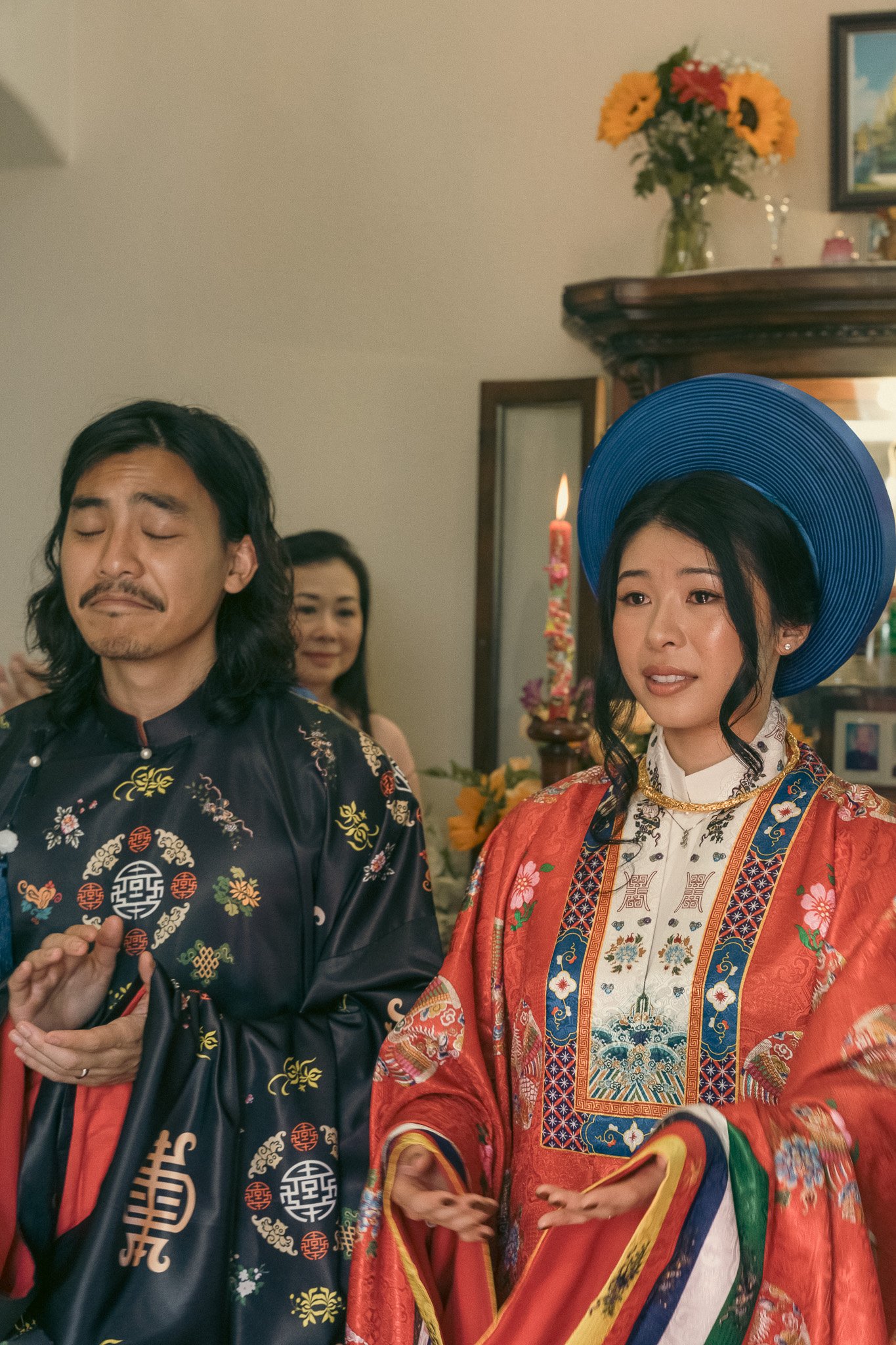 A couple in traditional East Asian attire performing a ceremony indoors.