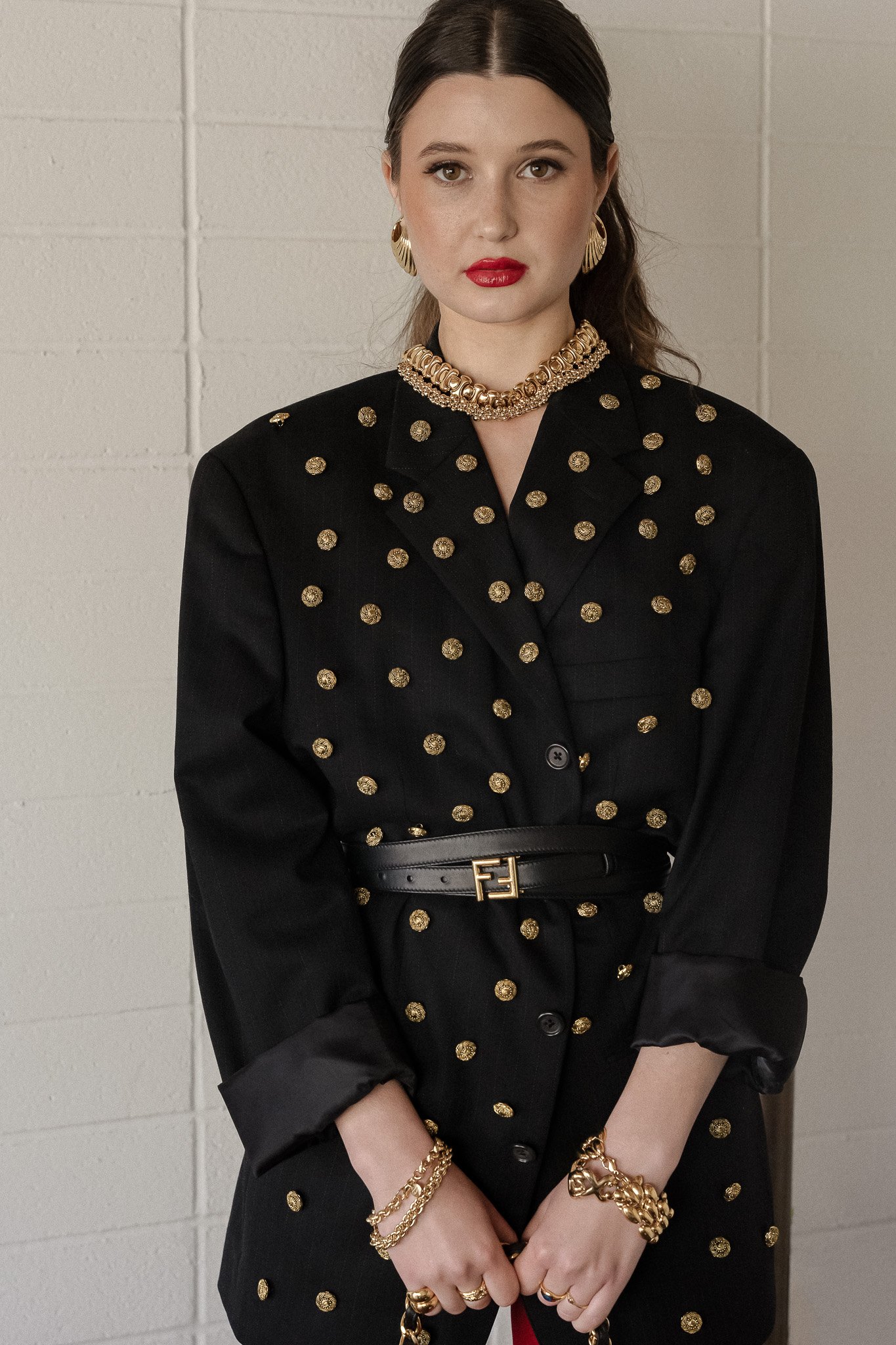 Woman wearing a black blazer with gold accents, gold jewelry, and red lipstick.