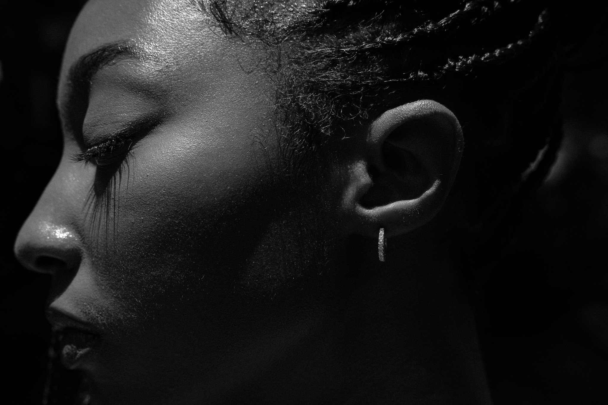 Black and white close-up profile of a person's face with braids, highlighting an ear with a hoop earring.