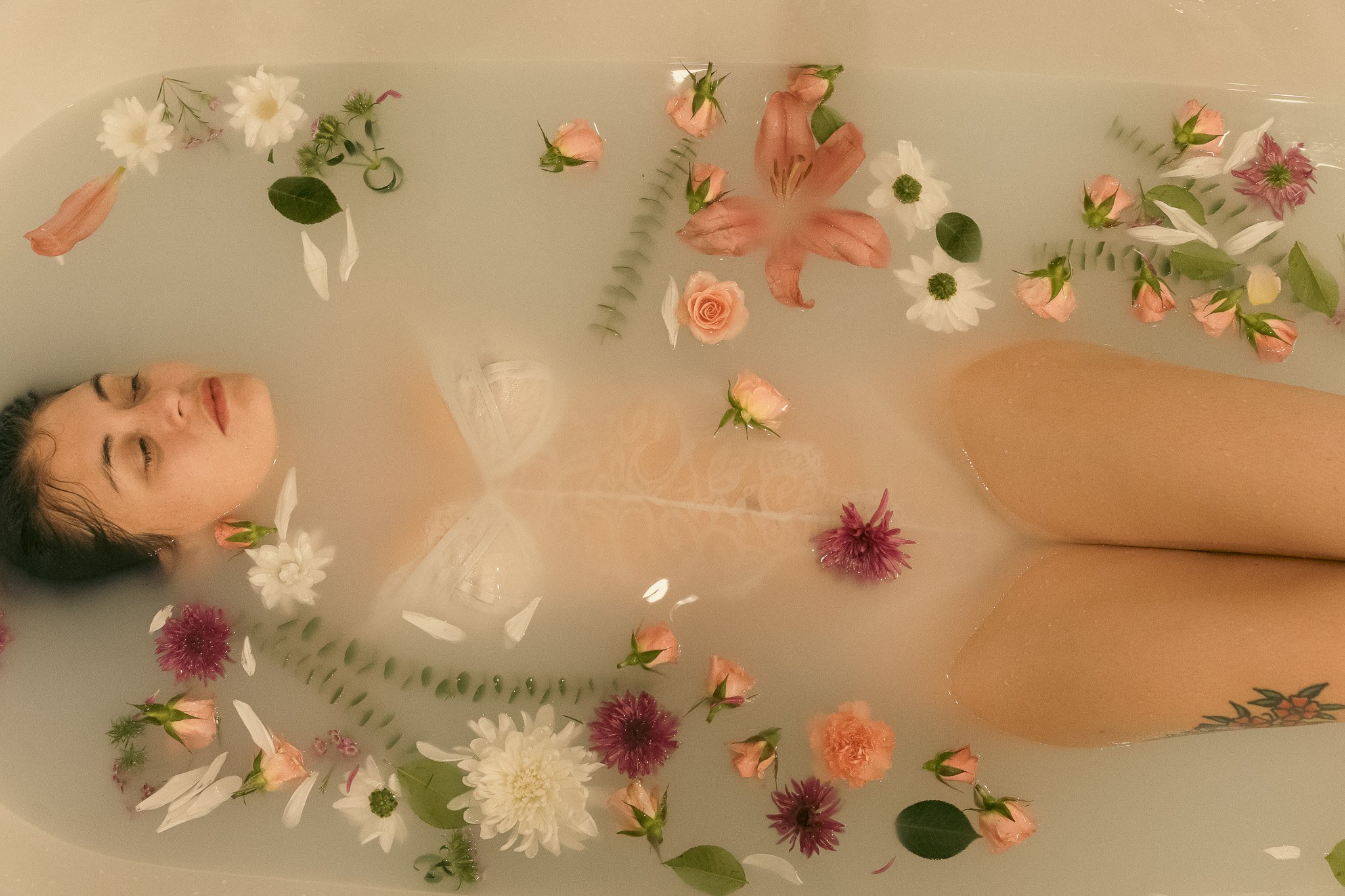 Woman lying in a milk bath with pink and white flowers