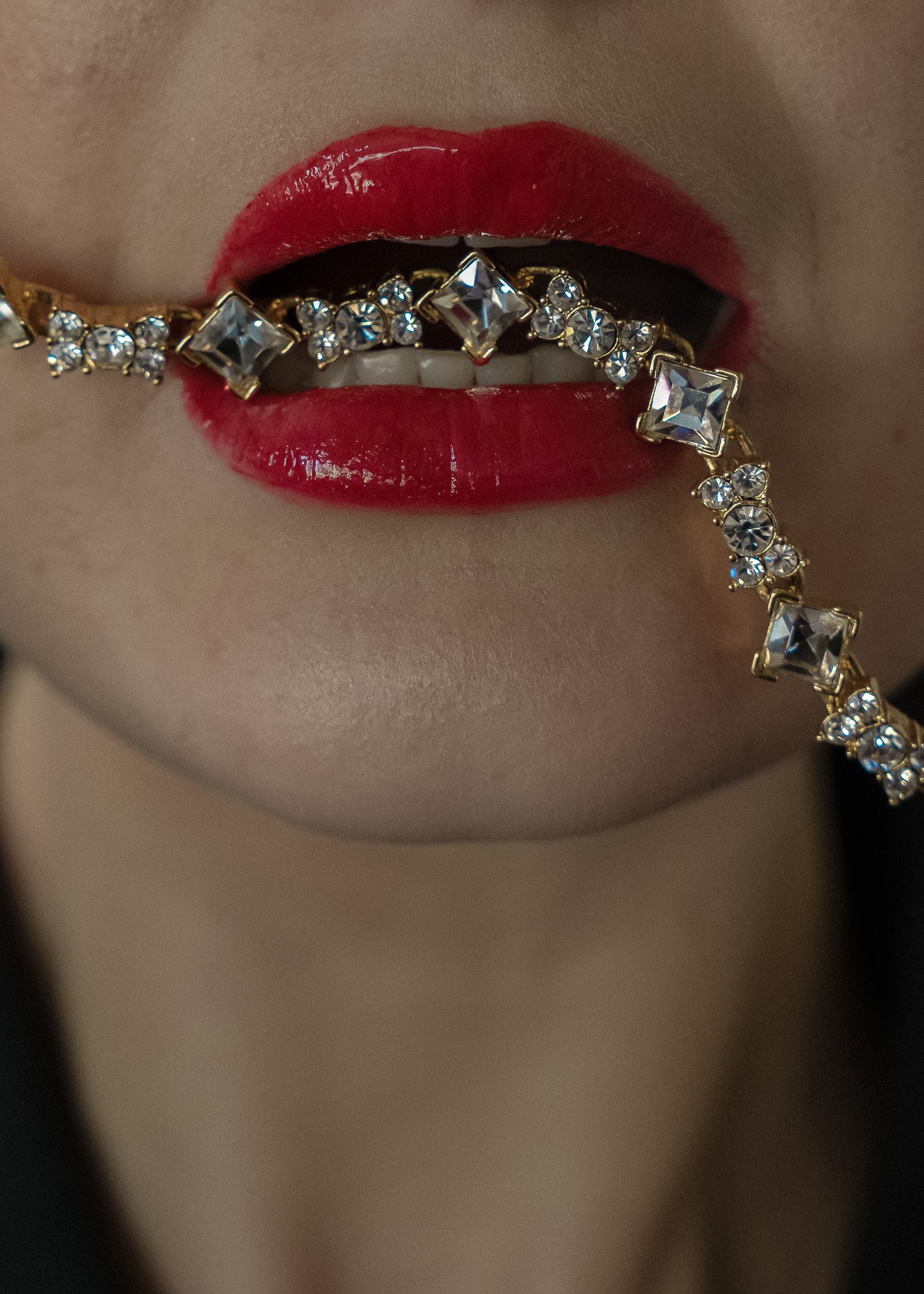 Woman with red lips holding a diamond necklace in her mouth.