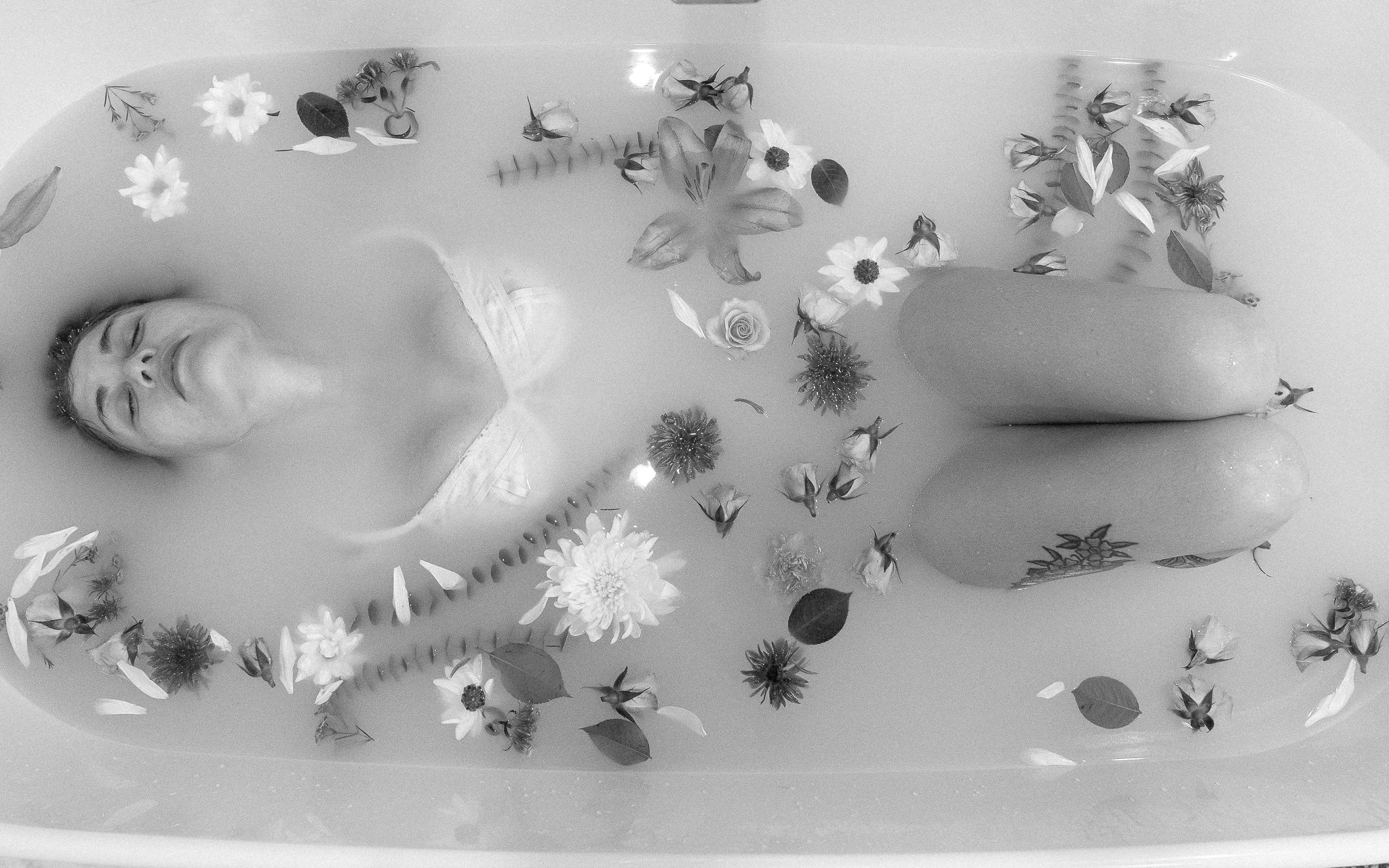 Person submerged in a milk bath with various flowers floating on the surface.