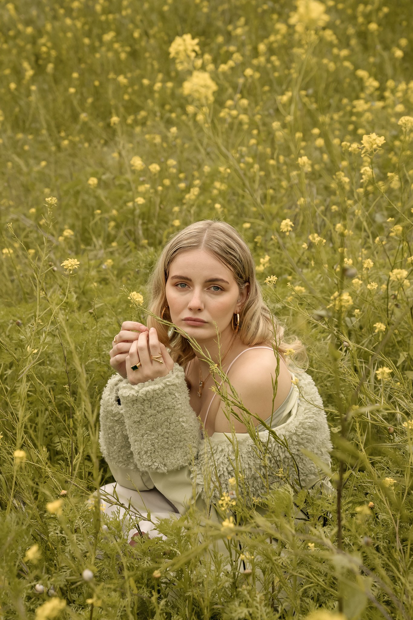 Woman sitting in a field of yellow flowers, wearing a green sweater.