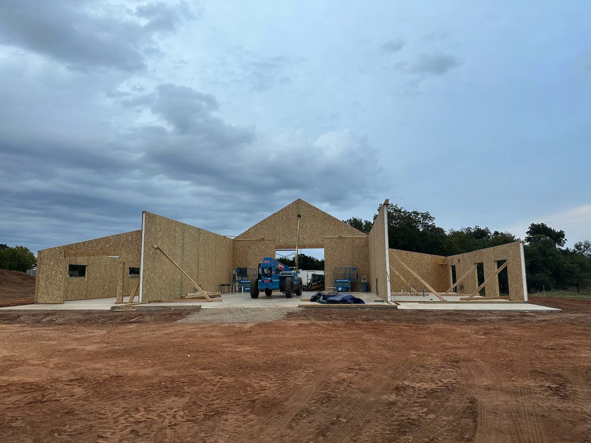 Three construction workers assembling an oriented strand board (OSB) wall panel on a building site under a clear sky.