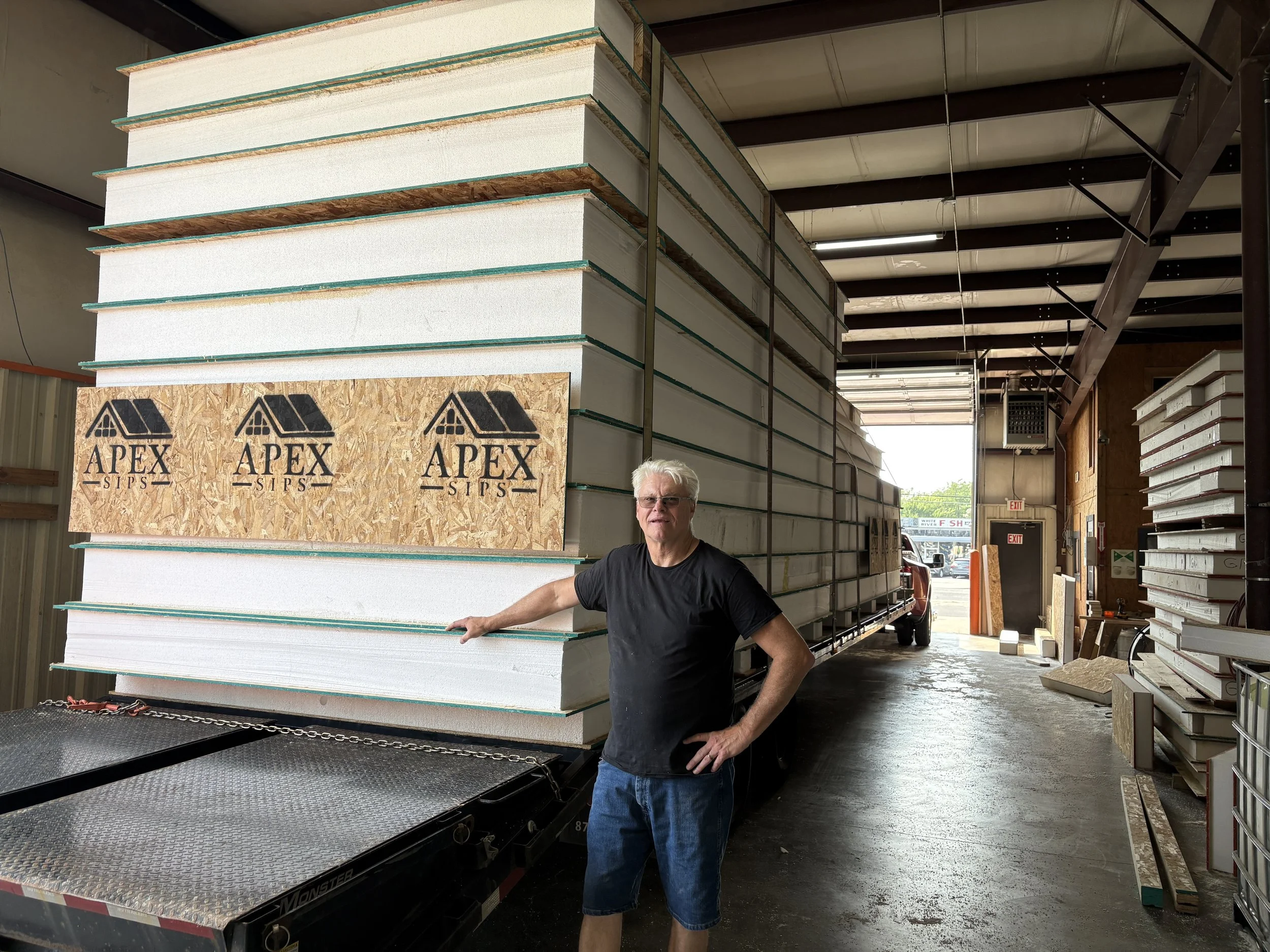 Modern building under construction with black metal siding, large windows, and construction materials in the foreground on a clear day.