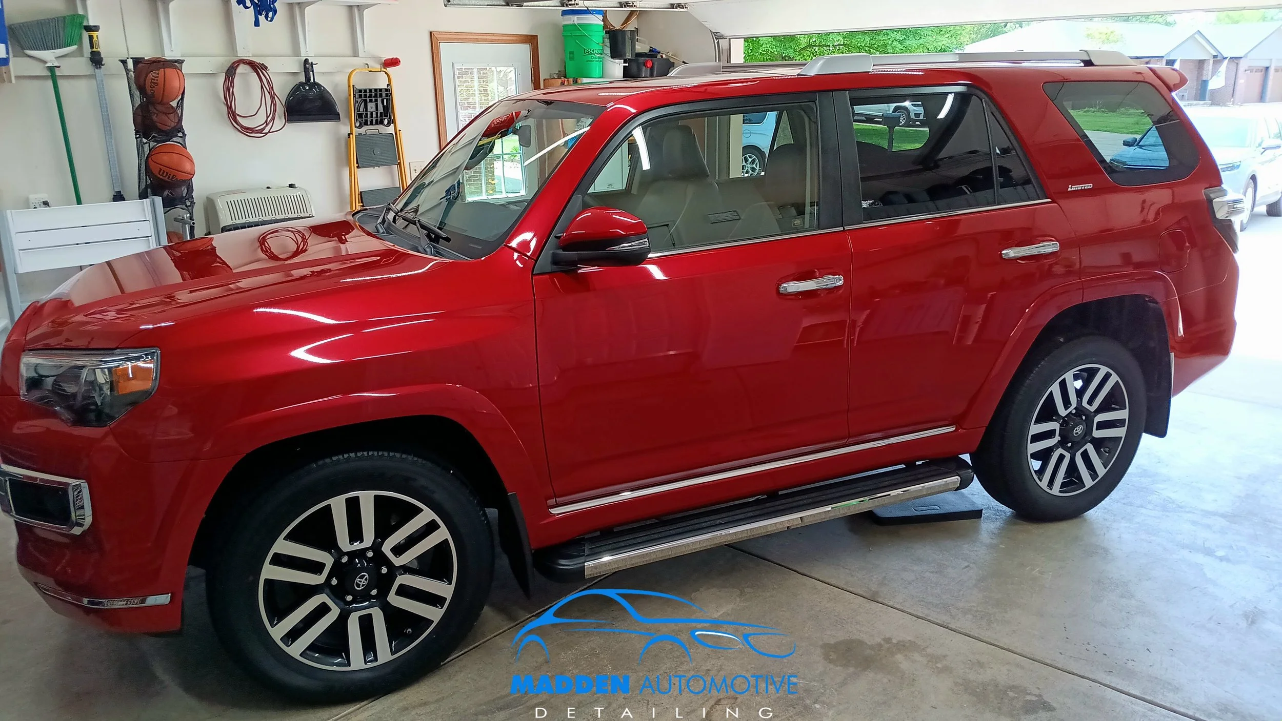 Red SUV parked inside a garage with tools and equipment hanging on the wall and a window showing the outdoors.