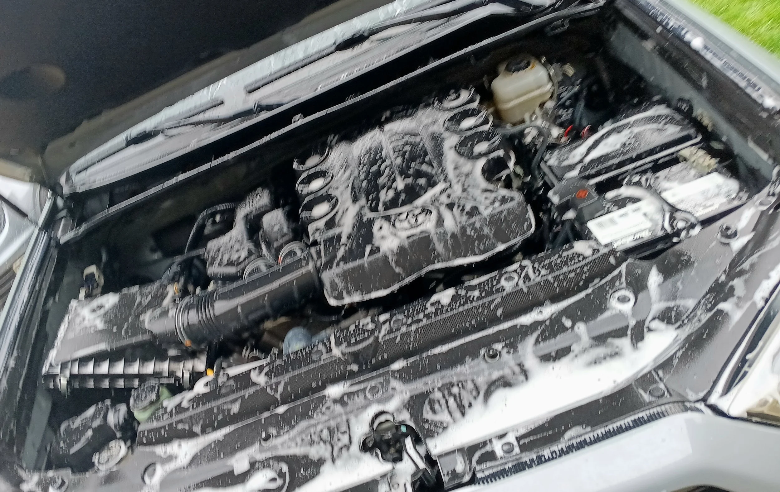 View of a car engine with soap foam on various components after cleaning.