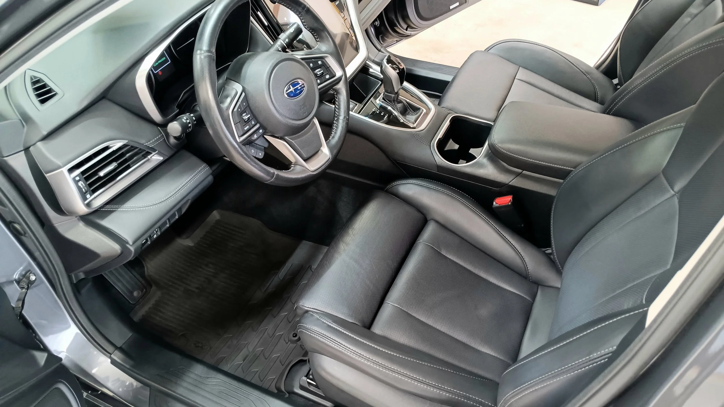 Interior of a vehicle, showing the steering wheel, dashboard, center console with gear shifter, and black leather seats with white stitching.