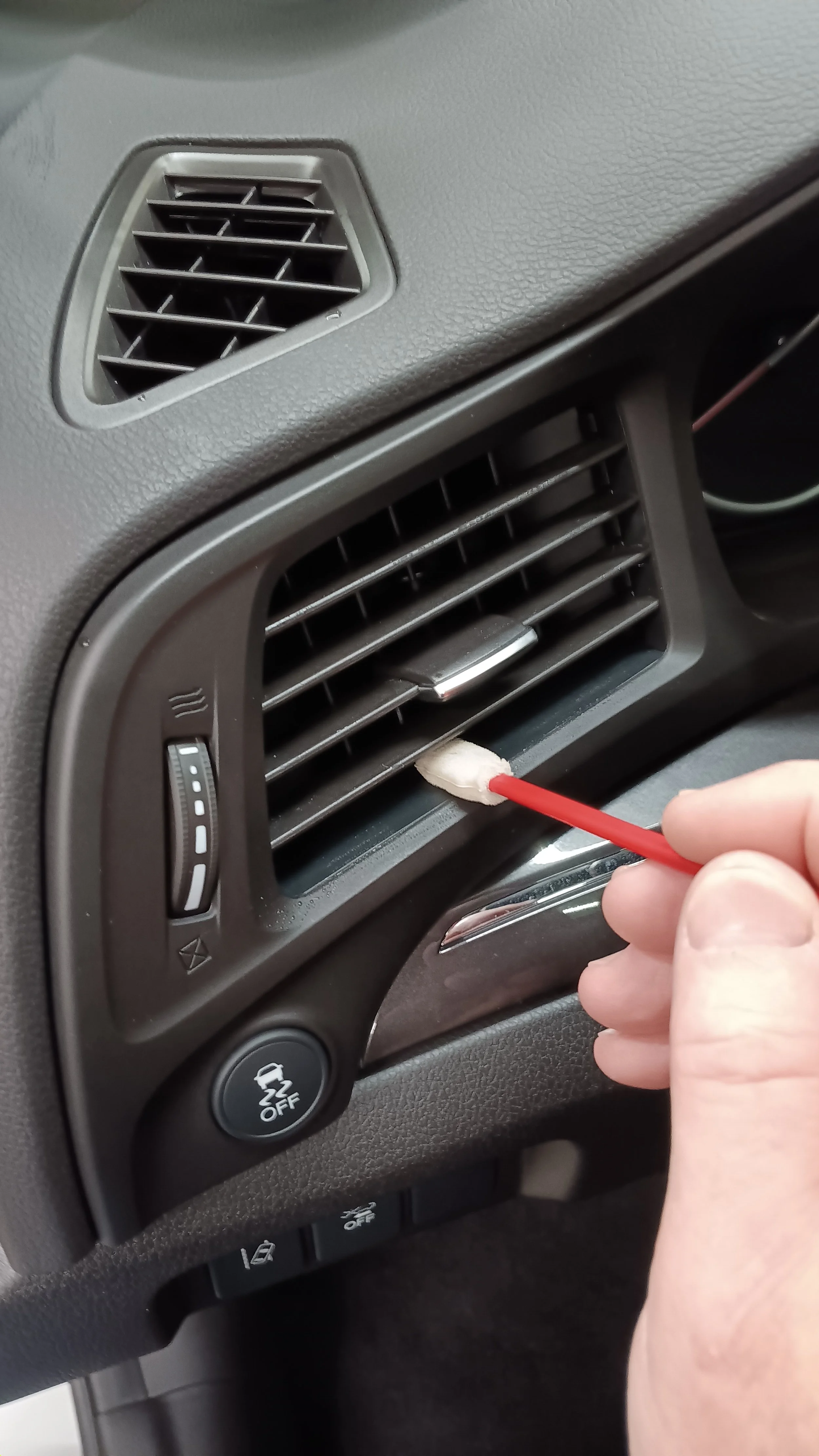Person using a cotton swab to clean the air vent of a car dashboard.