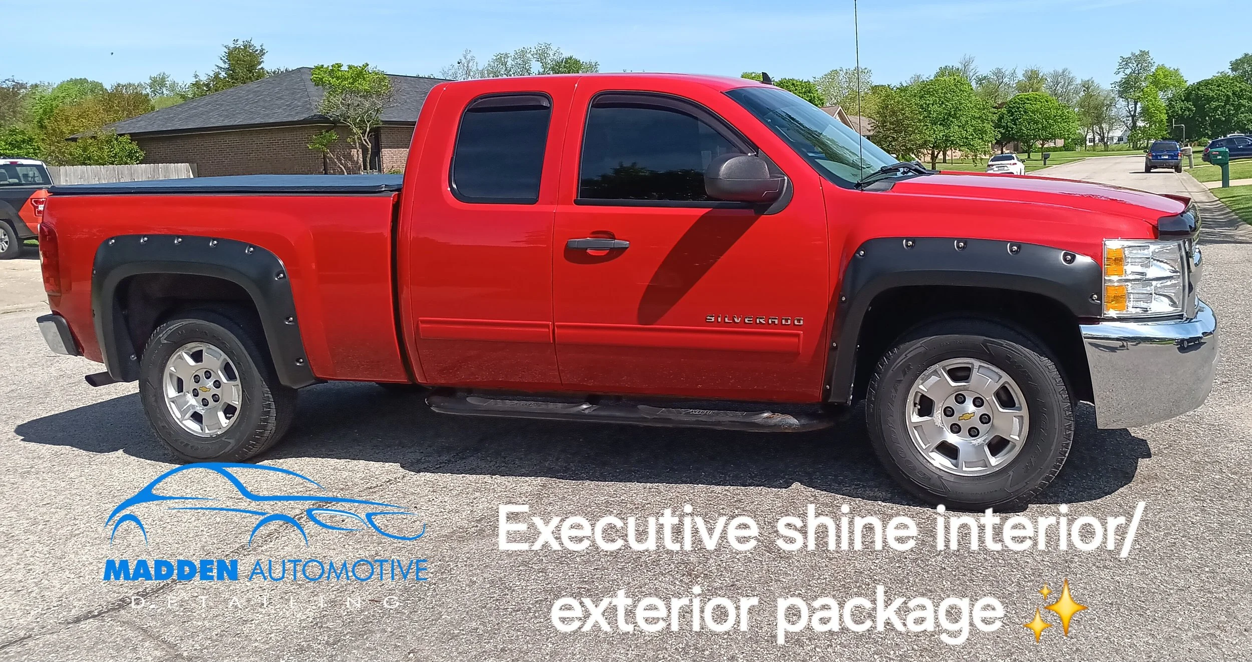 Red Chevrolet Silverado pickup truck with black fender flares and wheels, parked on a street in a suburban neighborhood, showcasing a shiny interior and exterior detailing.