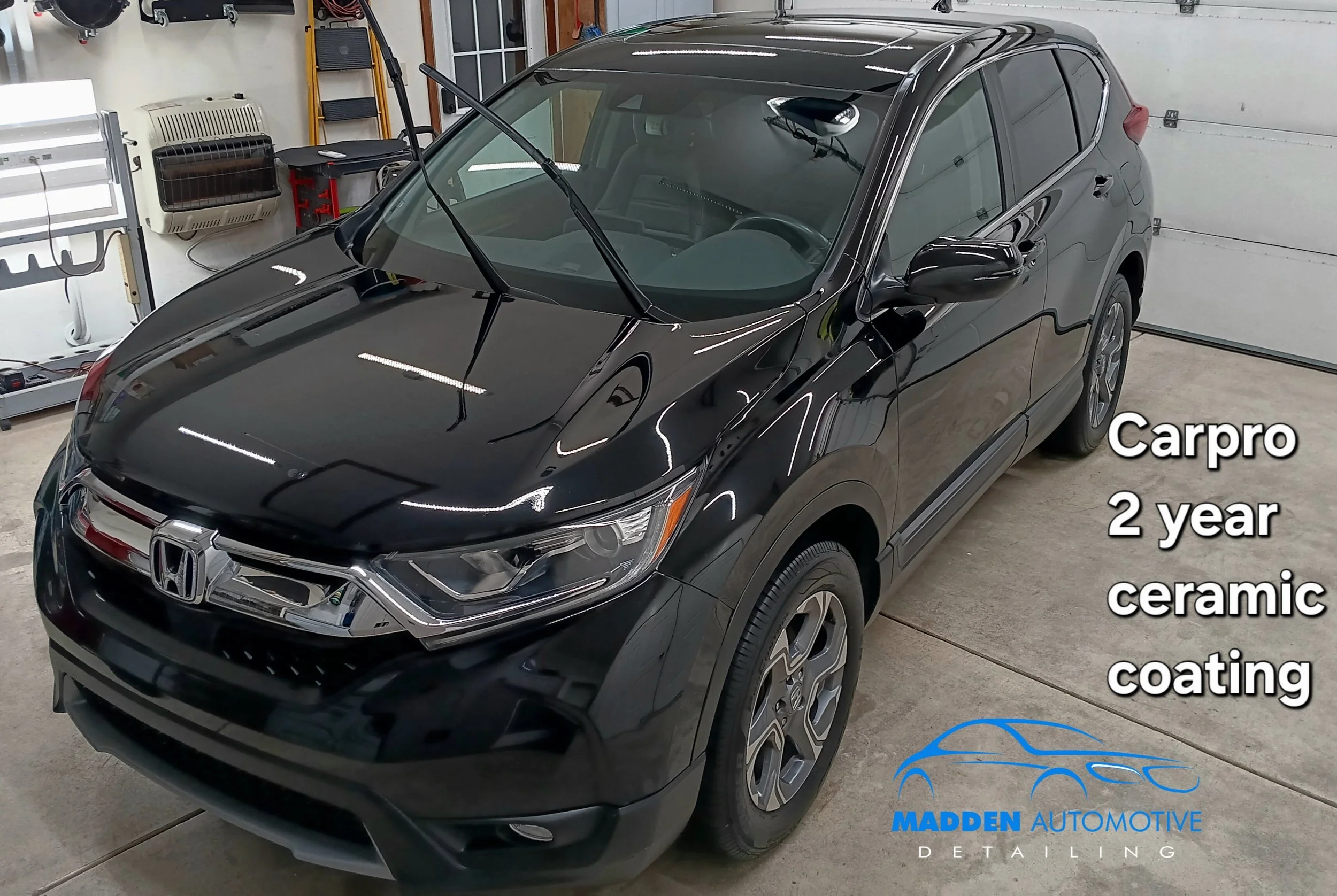 Black Honda SUV in a garage with auto detailing equipment, windshield wipers lifted, and a logo for Madden Automotive Detailing.