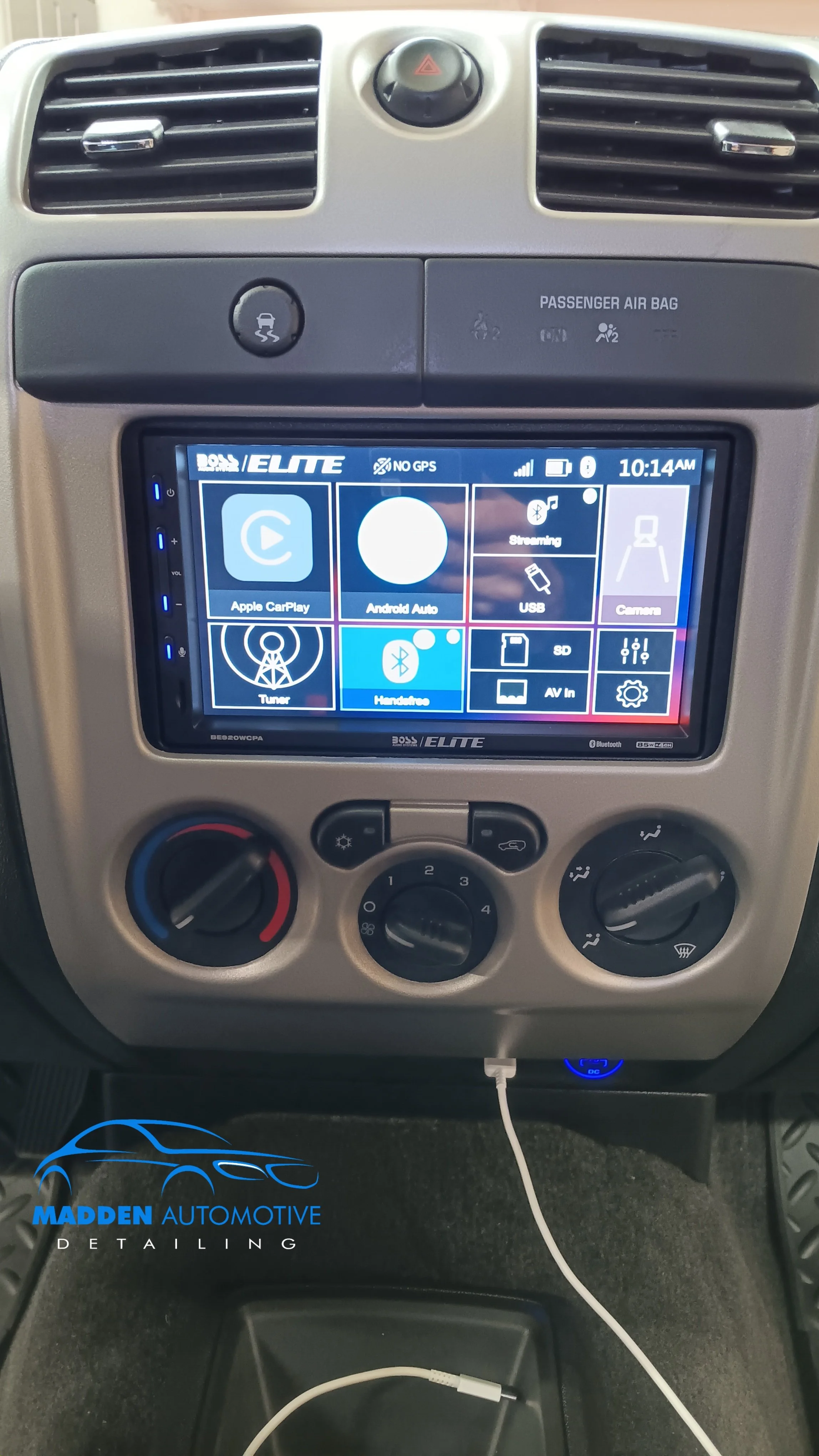 Car dashboard with a touchscreen display showing options like Apple CarPlay, Android Auto, USB, Tuner, Bluetooth, and Camera, surrounded by climate control dials and vents.