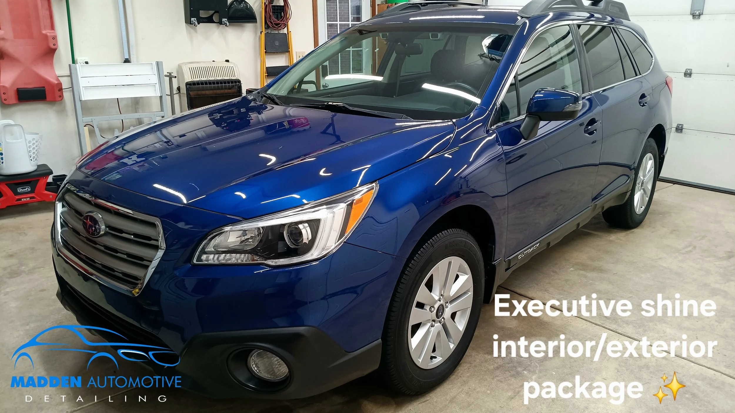 A blue Subaru Outback inside a garage. The garage has various tools and equipment on the walls. The car has a shiny exterior, and the image includes text promoting a detailing package from Madden Automotive. 