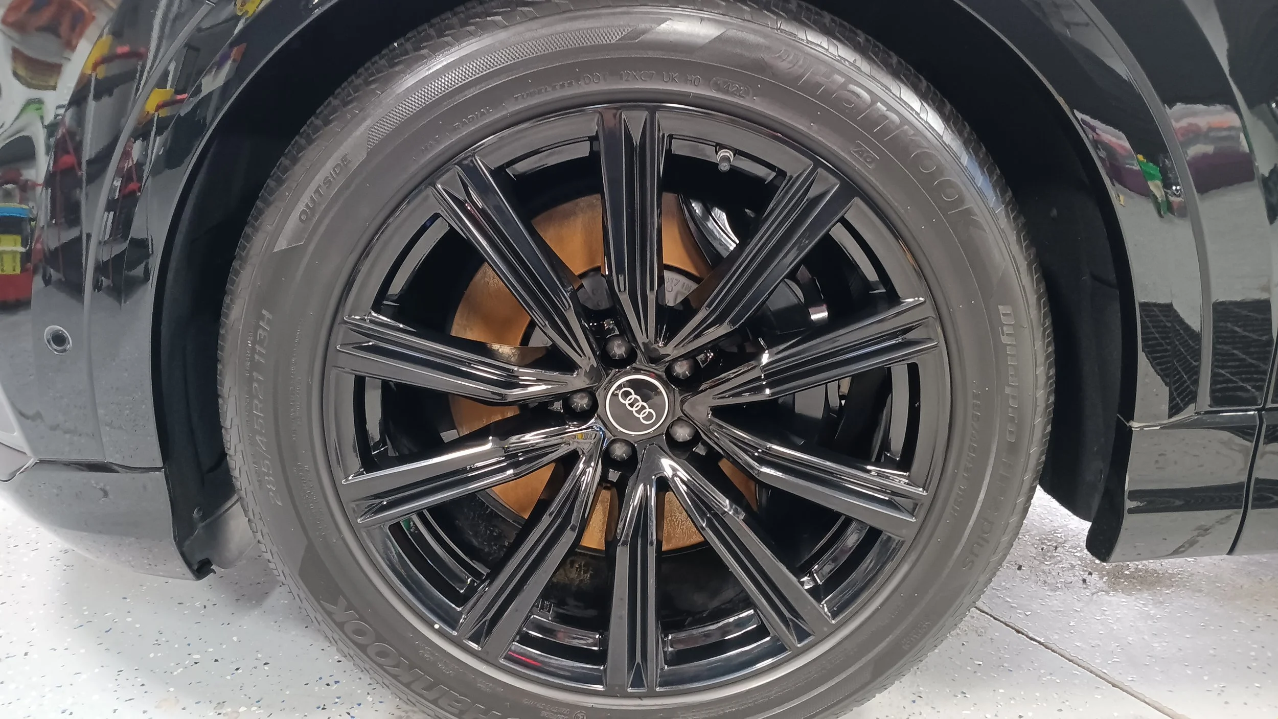 Close-up of a black car wheel with a shiny, multi-spoke alloy rim and the Audi logo at the center. The tire is a Goodyear Eagle F1 Asymmetric 3, with visible tread pattern and sidewall markings.