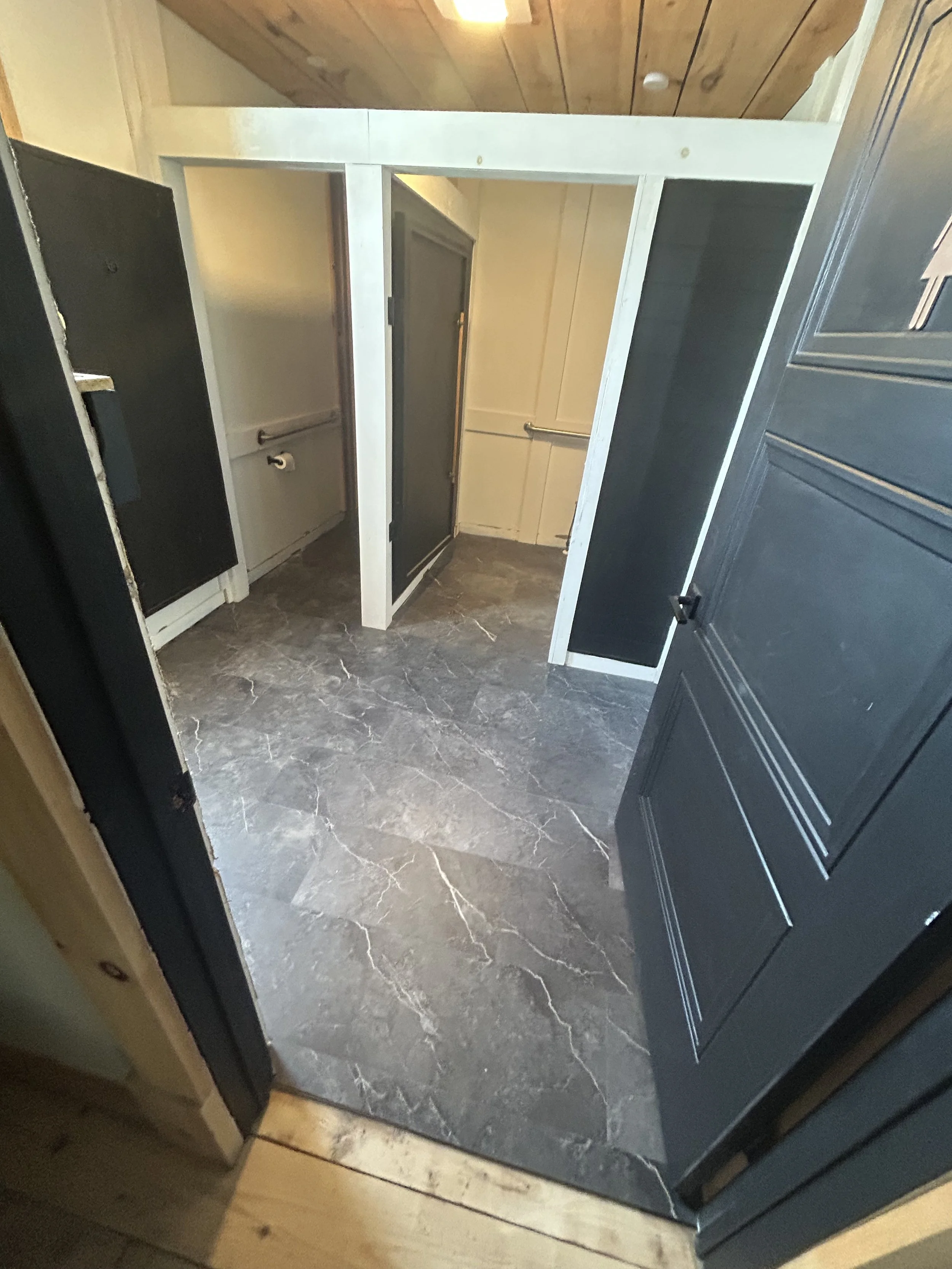 Small enclosed room with dark gray doors, tile flooring, and partial view of wooden ceiling.
