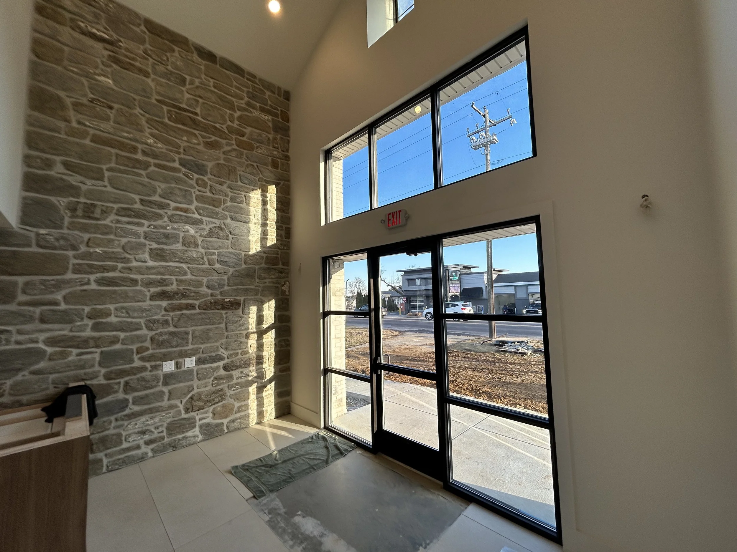 Interior of a modern building entrance with large glass doors and windows, stone accent wall, and a sidewalk view outside.