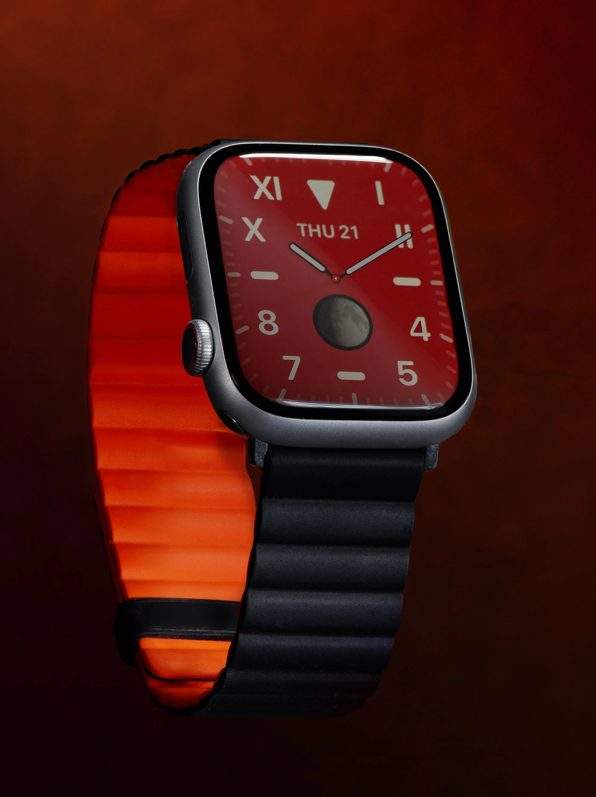 A smartwatch with a red and black band, displaying a red dial with the time, date, and moon phase on its screen.