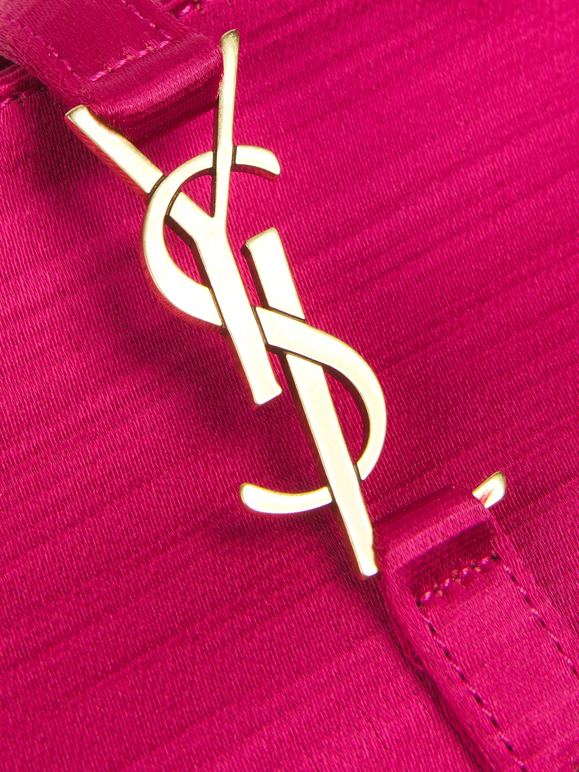 Close-up of a gold YSL logo on a pink fabric background.