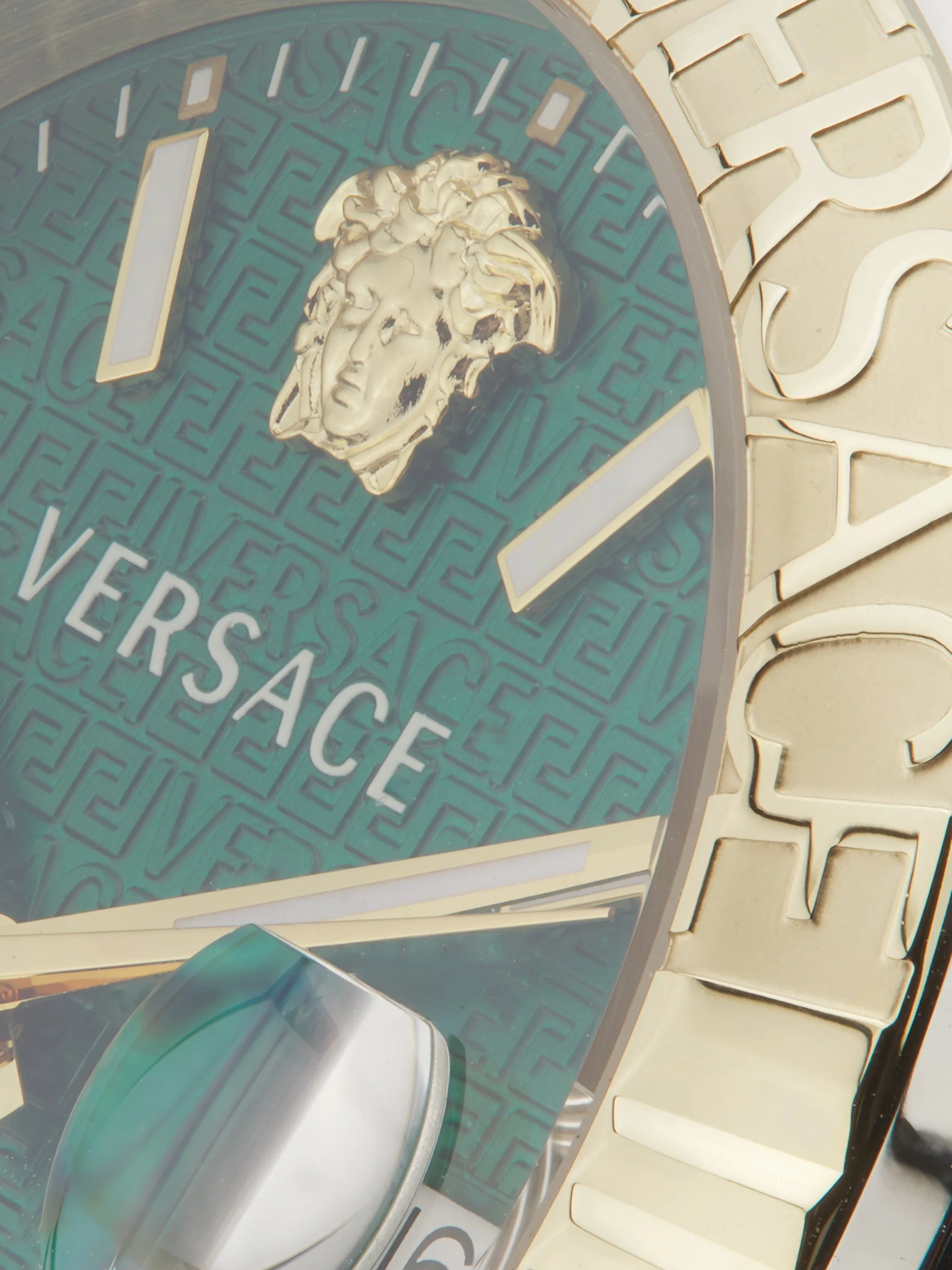 Close-up of a Versace watch face with a golden lion head emblem and the brand name Versace; part of a gold bracelet is visible.