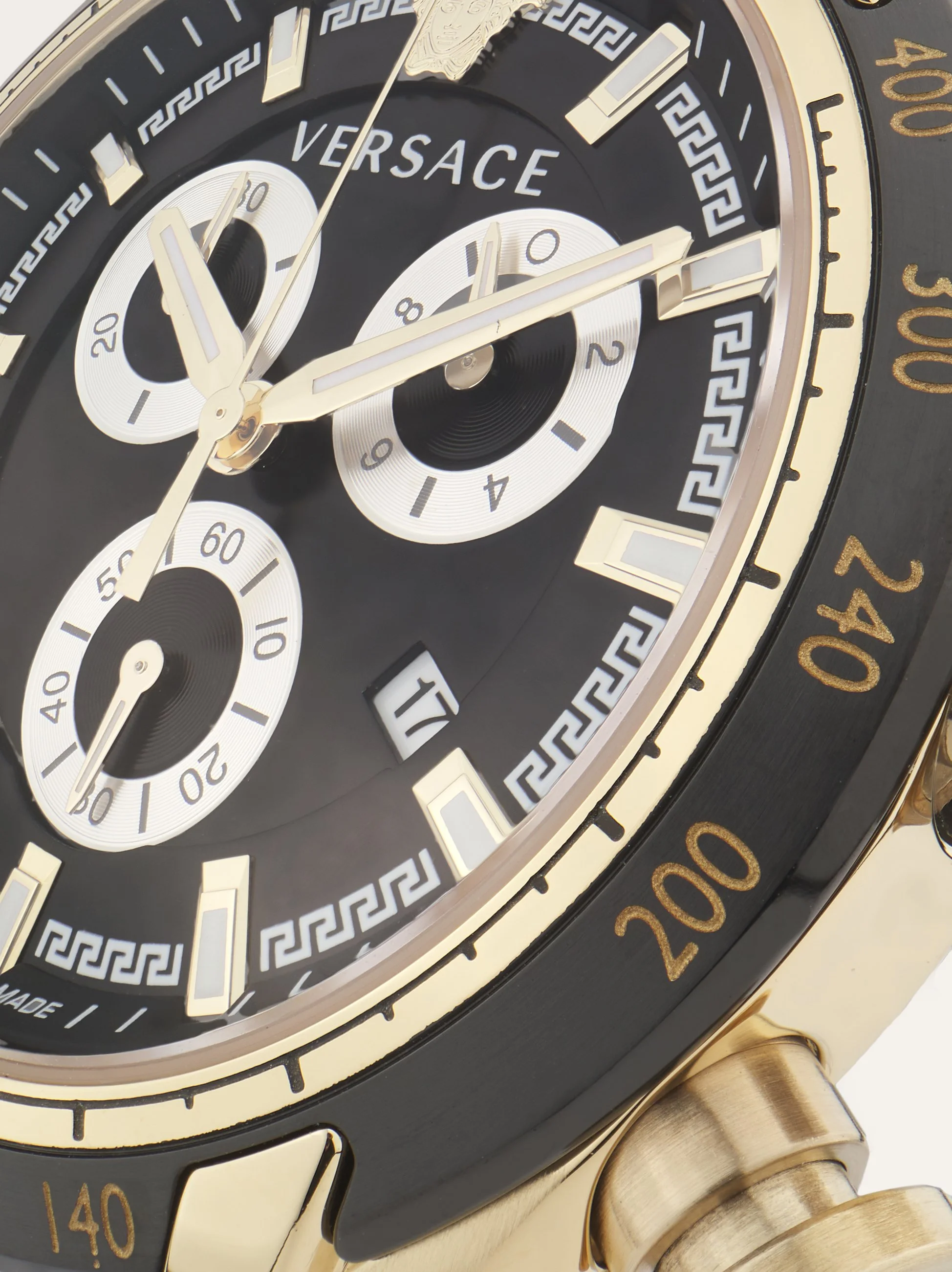 A luxury Versace wristwatch with a black and gold design, featuring multiple subdials, a date window, and Greek key patterns on the face.