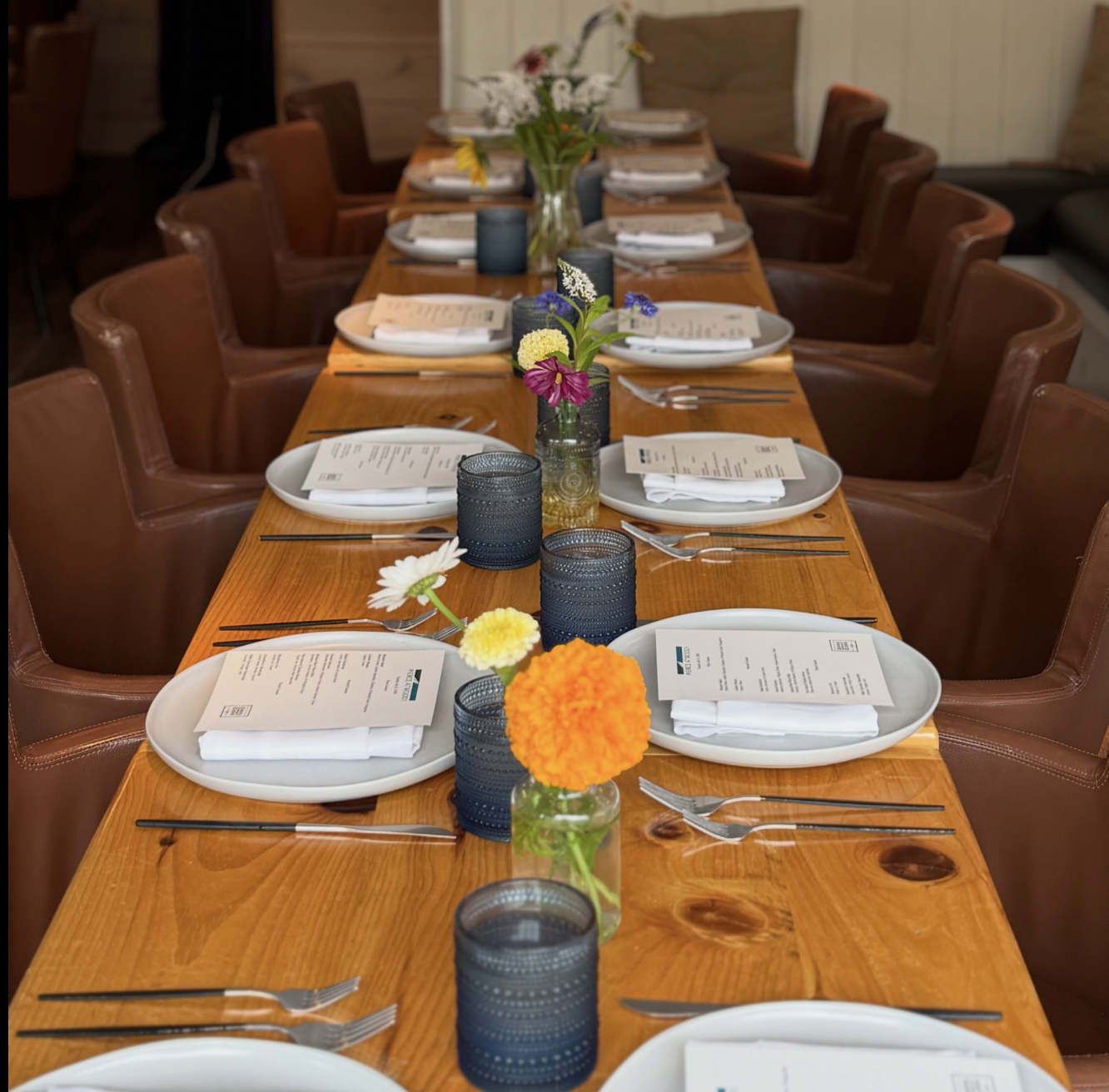 A beautifulTables in our café space set with fresh flowers, white plates, blue glasses, and brown leather chairs