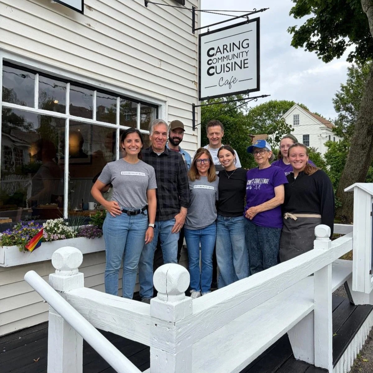 People smiling and standing on the deck outside Caring Community Cuisine café
