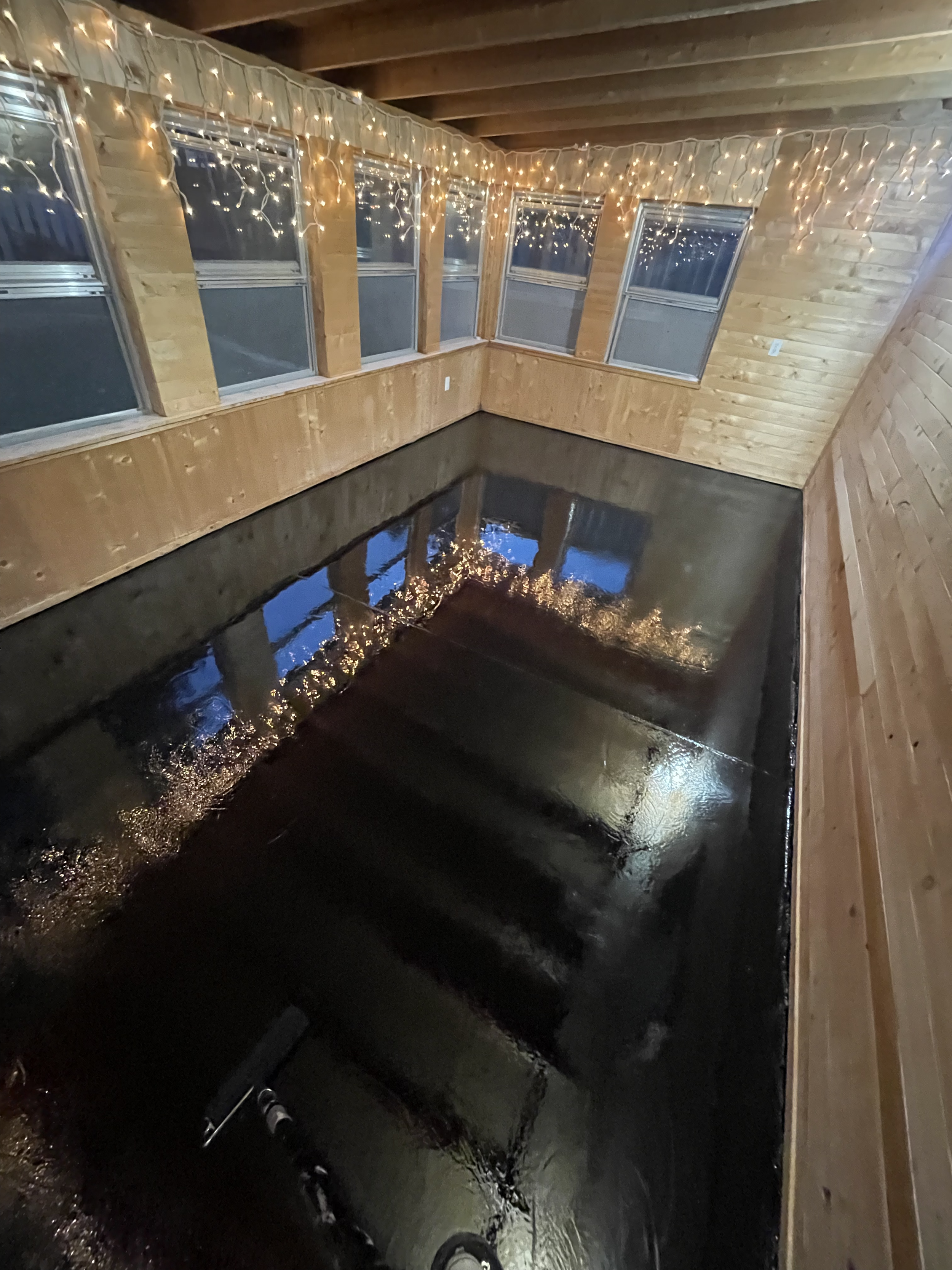 Room with dark, glossy floor, wooden walls, and string lights. Epoxy services in Winnipeg.