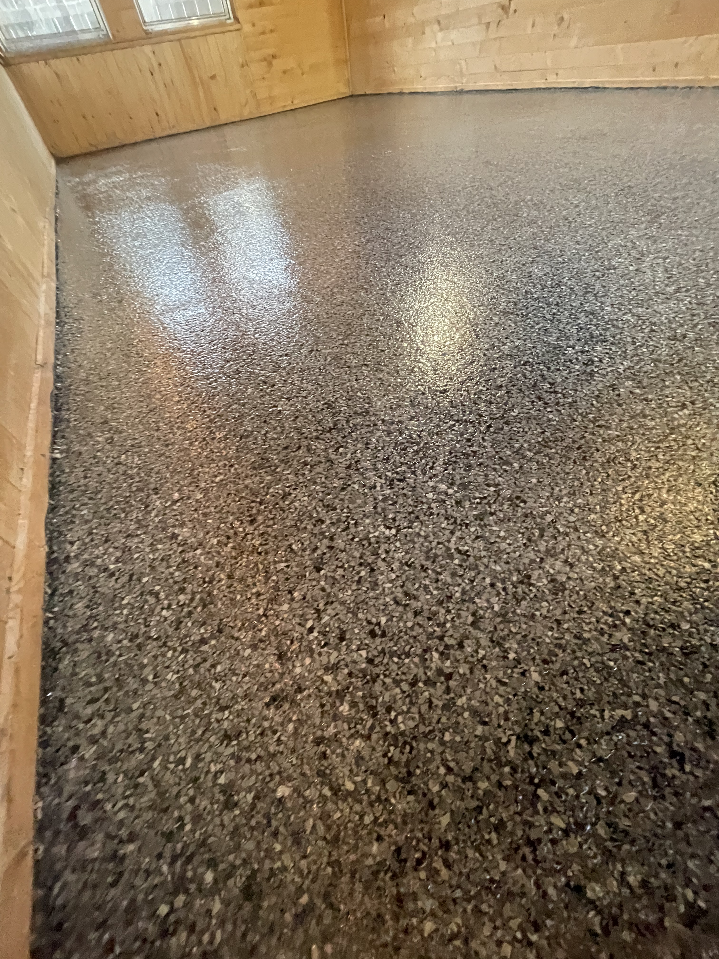 A room with a shiny, gray speckled epoxy floor and wooden walls with vertical paneling. Epoxy services in Winnipeg.